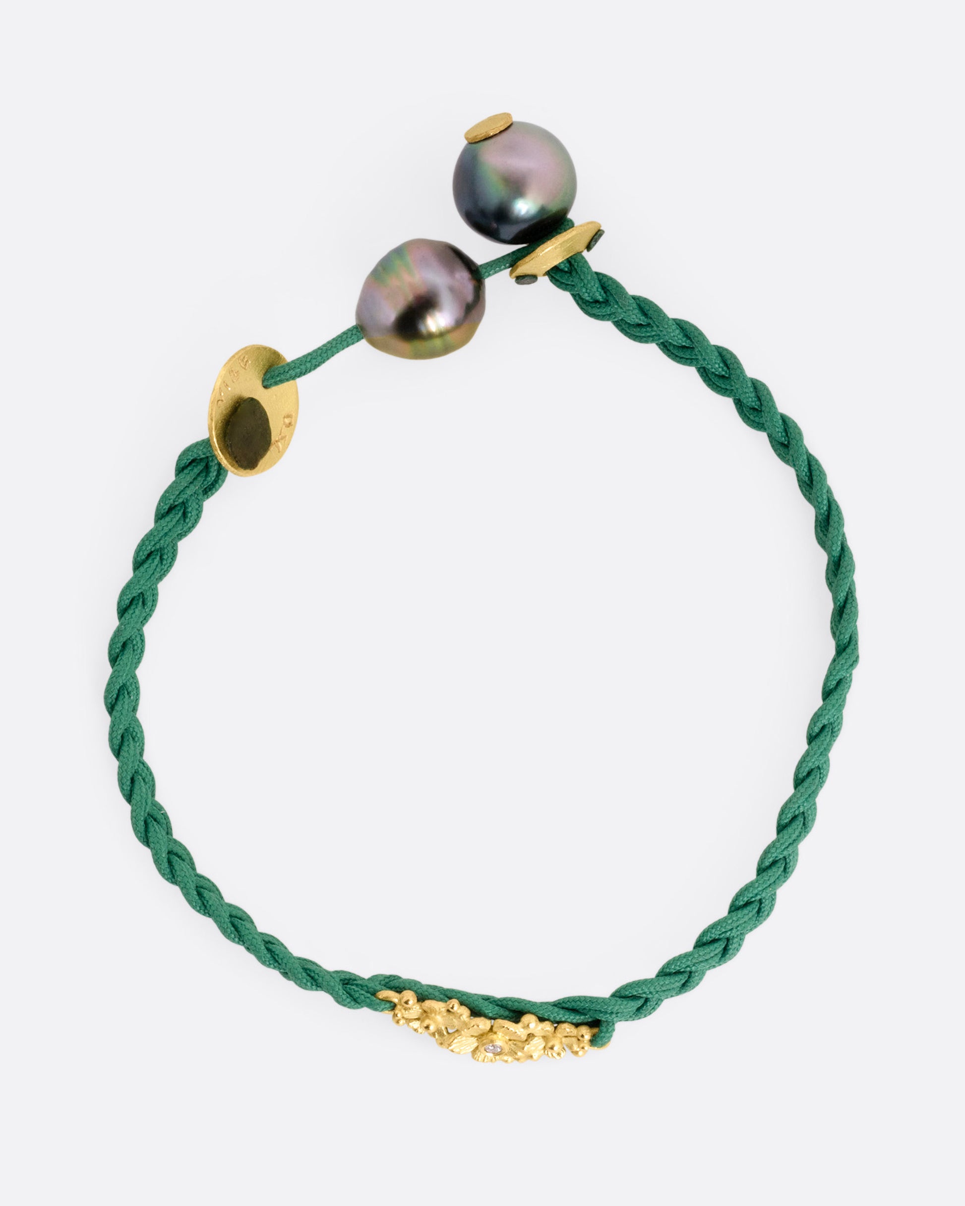 A braided green cord bracelet with a yellow gold cluster of diamond accented flowers and a Tahitian pearl toggle closure. Shown from the top.