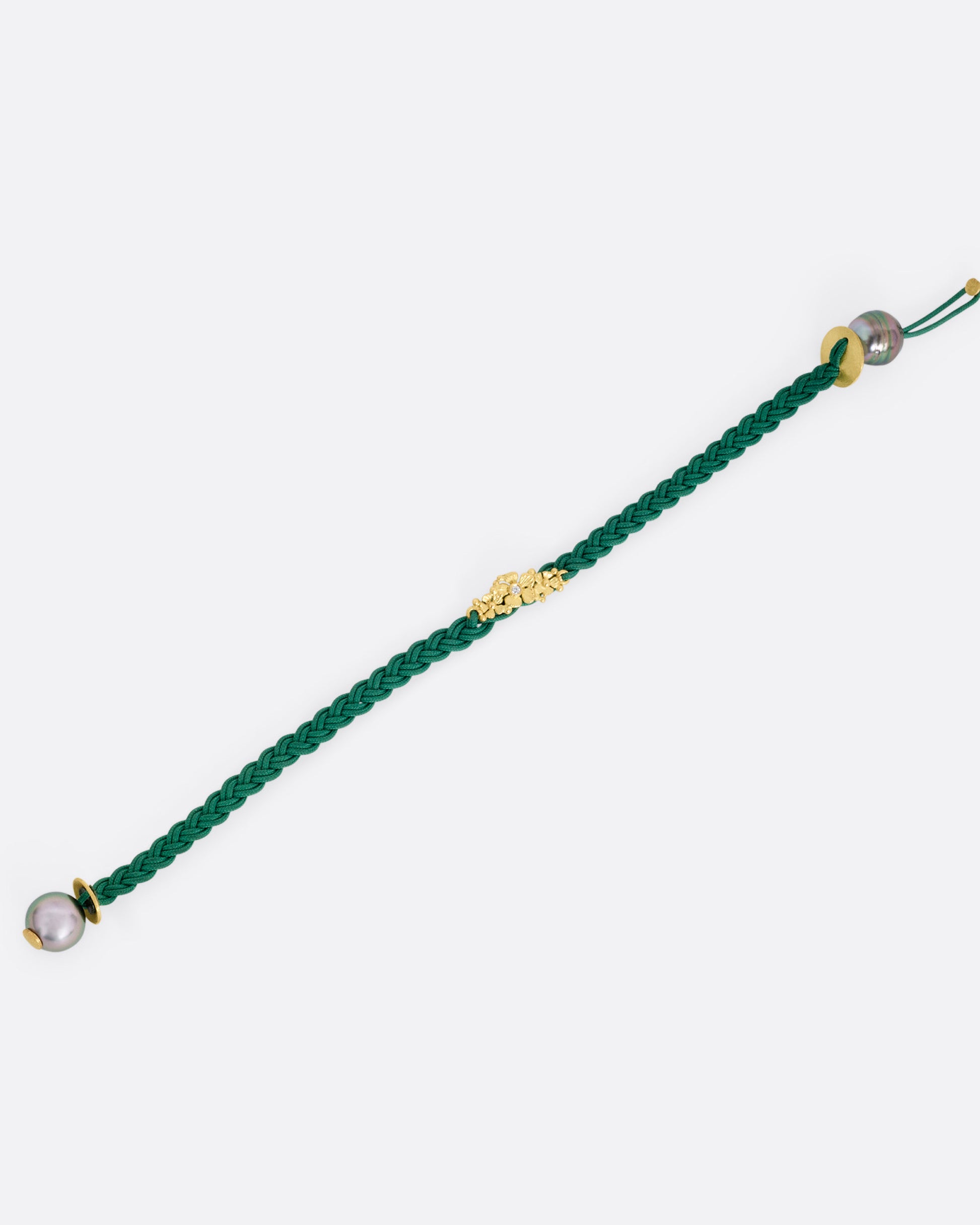 A braided green cord bracelet with a yellow gold cluster of diamond accented flowers and a Tahitian pearl toggle closure. Shown from the front open.