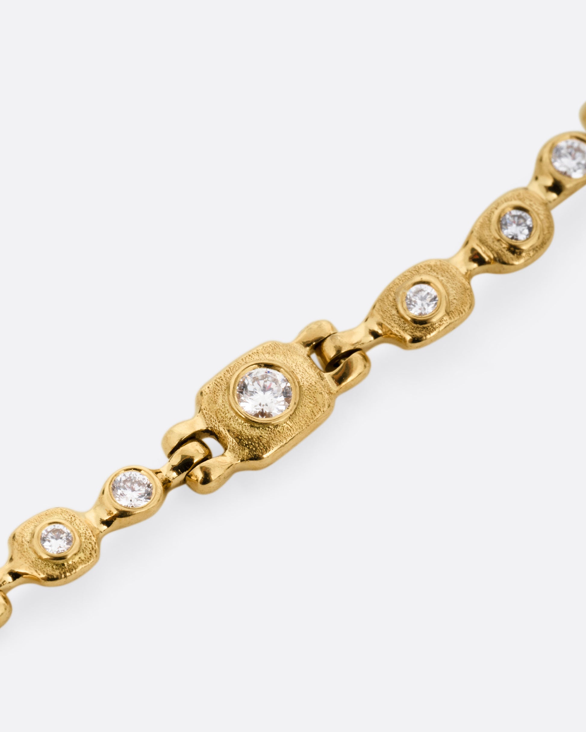 A close up of a yellow gold linked necklace with diamonds, shown from the front.