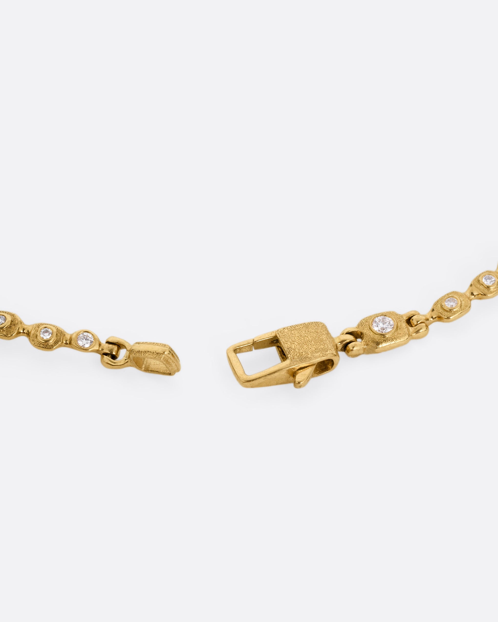 A close up of the clasp on a yellow gold linked necklace with diamonds, shown open.