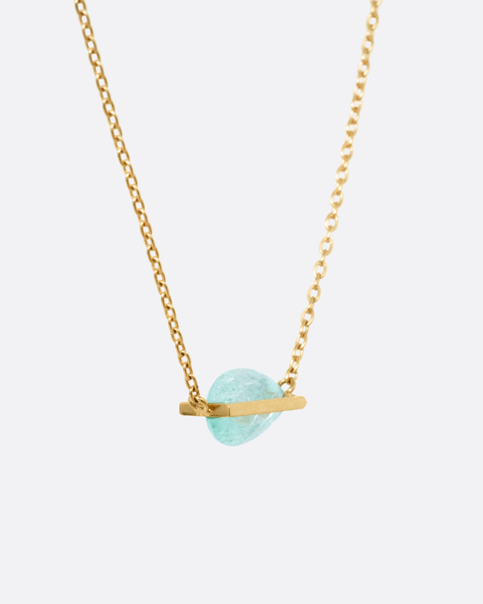 A yellow gold cable chain necklace with a blue-green Paraiba tourmaline pendant, shown from the side.