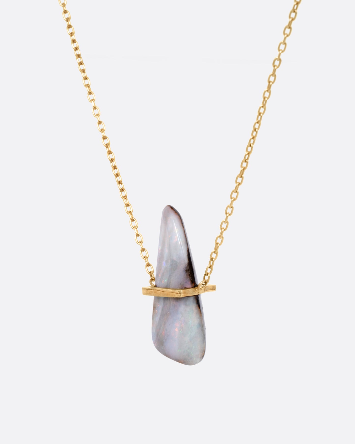 A yellow gold necklace with a freeform opal pendant, shown from the side.