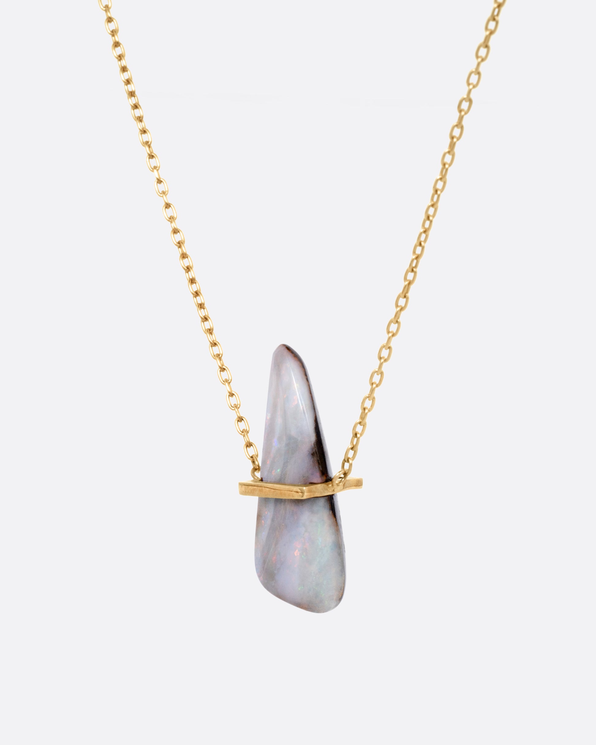 A yellow gold necklace with a freeform opal pendant, shown from the side.