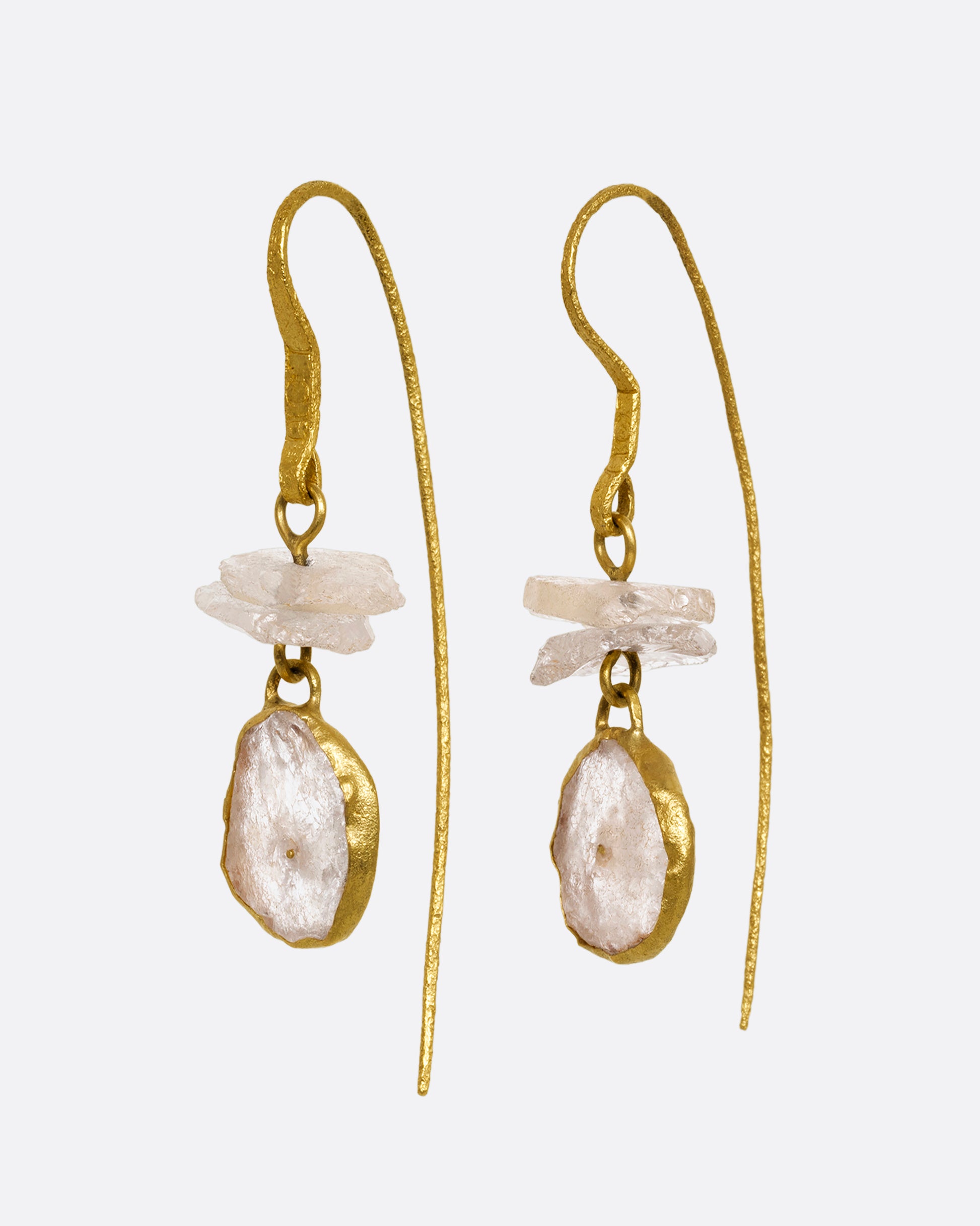 A pair of earrings with white quartz stacks, yellow gold ear hooks, and two front- facing gold wrapped quartz slices. Shown from the side.
