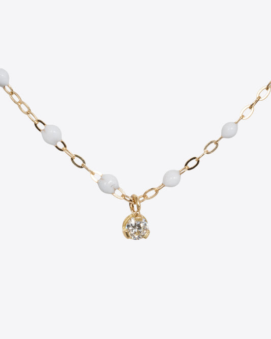 A close up shot of a yellow gold cable chain necklace with droplets of white resin and a single white diamond. Shown from the front.