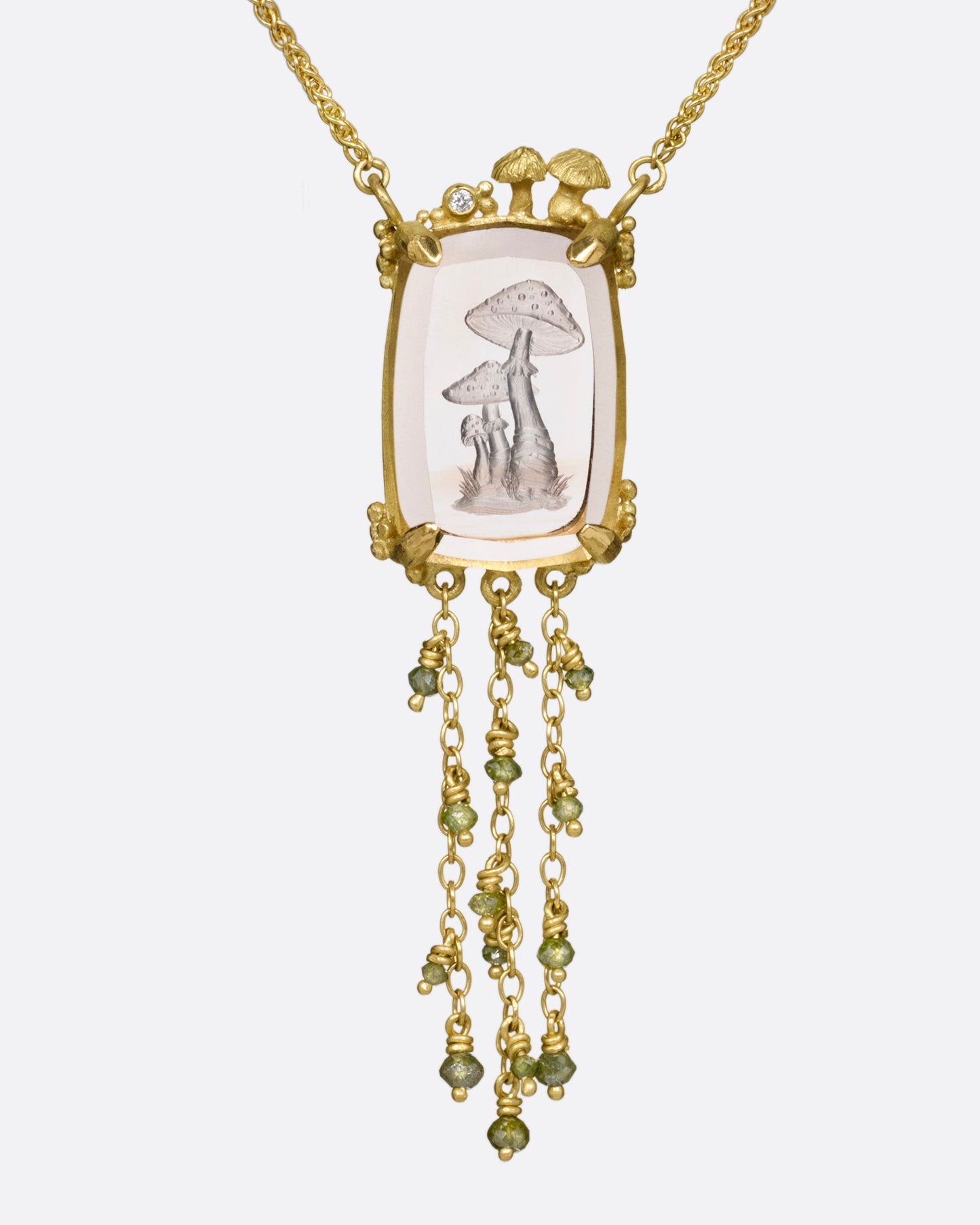 A yellow gold pendant necklace with a hand carved cluster of mushrooms in a light pink topaz with gold mushrooms and a diamond at the top edge. Three gold chains with green diamond beads hand from its base. Shown from the front.