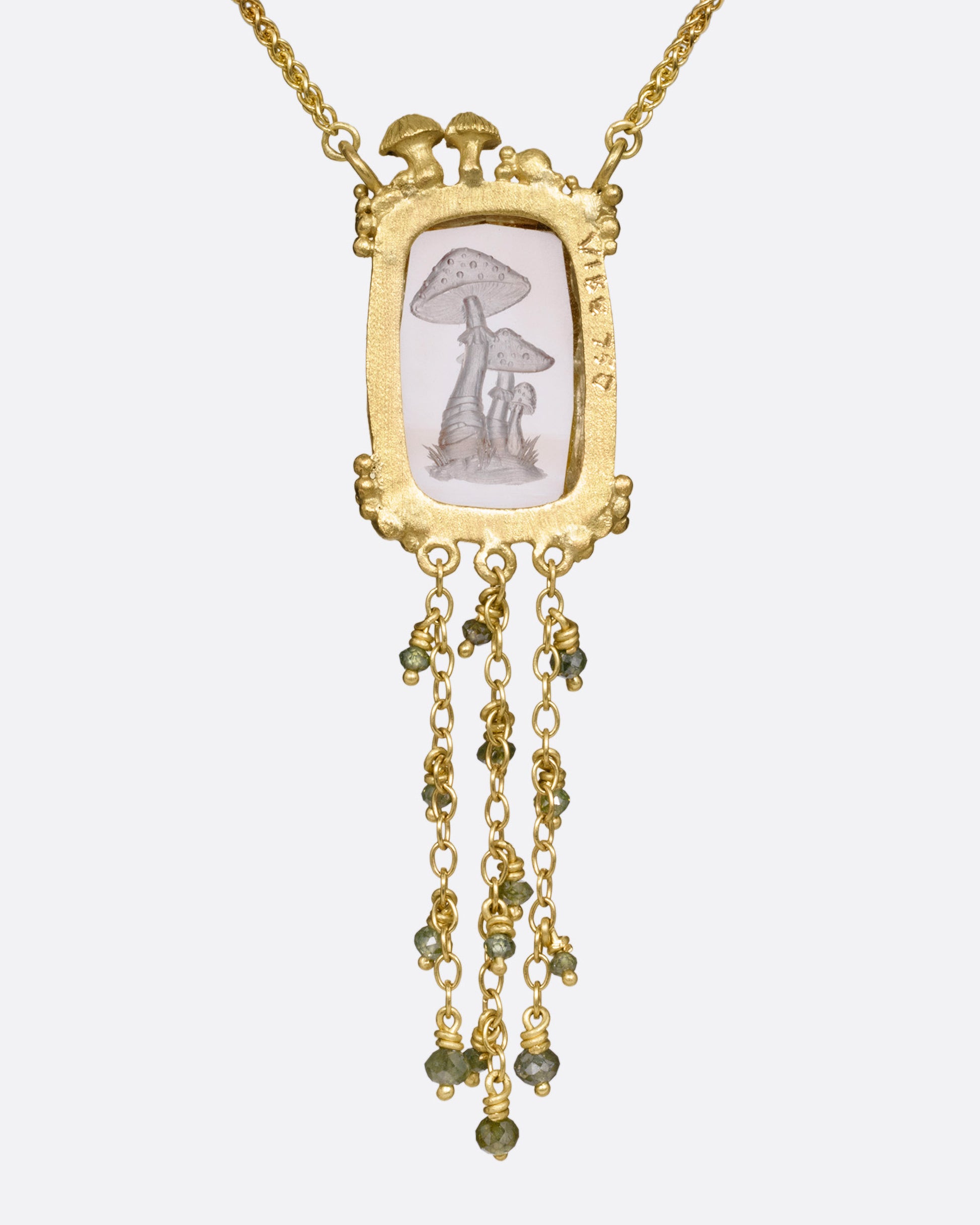 A yellow gold pendant necklace with a hand carved cluster of mushrooms in a light pink topaz with gold mushrooms and a diamond at the top edge. Three gold chains with green diamond beads hand from its base. Shown from the back.