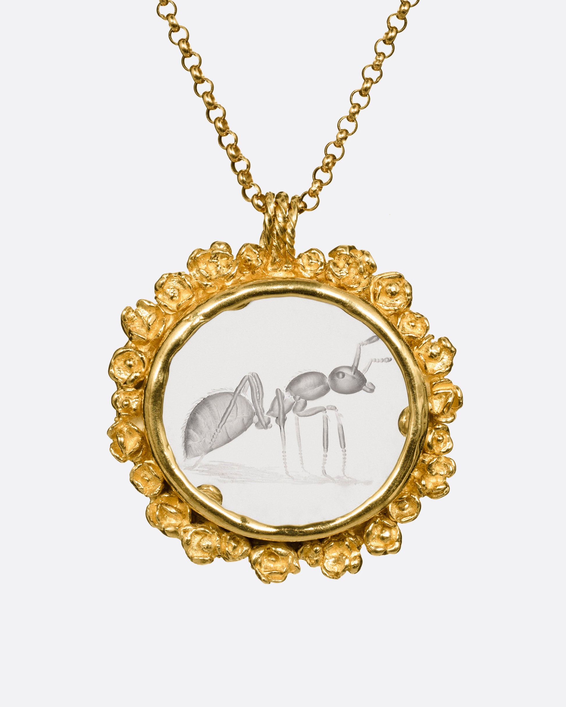 A yellow gold pendant necklace with a split bail and a quartz with a hand carved ant and a gold flower wreath along its edge. Shown from the front.