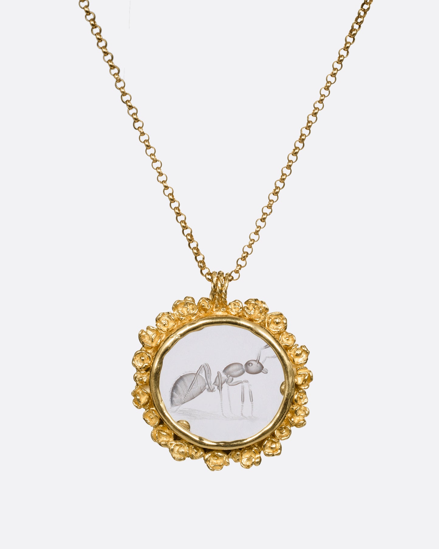 A yellow gold pendant necklace with a split bail and a quartz with a hand carved ant and a gold flower wreath along its edge. Shown from the front.