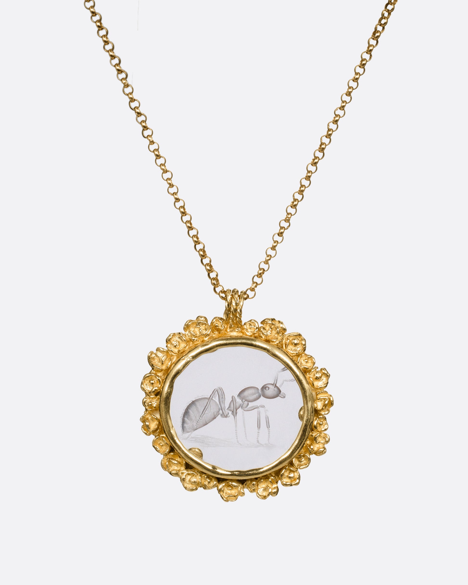 A yellow gold pendant necklace with a split bail and a quartz with a hand carved ant and a gold flower wreath along its edge. Shown from the front.