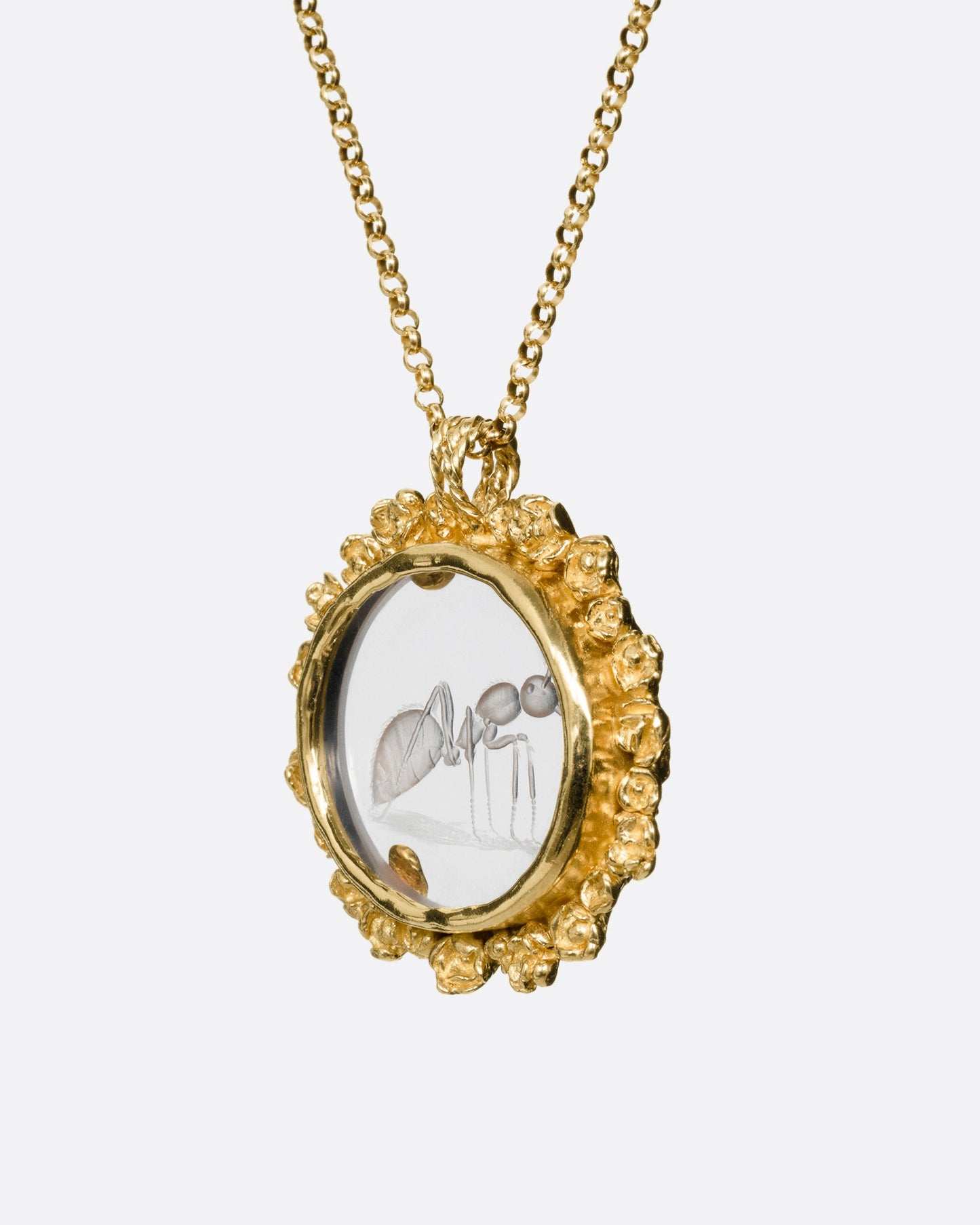 A yellow gold pendant necklace with a split bail and a quartz with a hand carved ant and a gold flower wreath along its edge. Shown from the side.