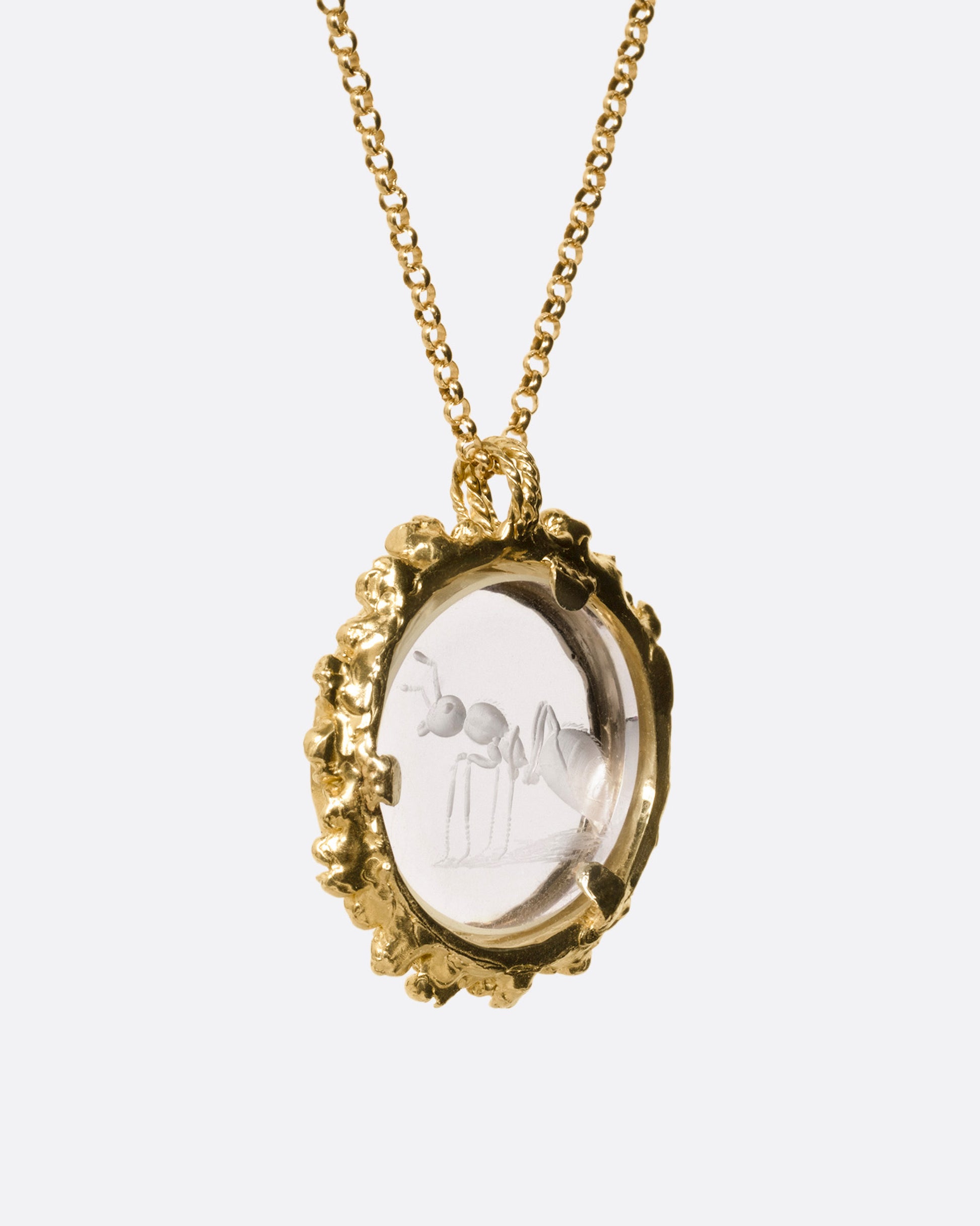 A yellow gold pendant necklace with a split bail and a quartz with a hand carved ant and a gold flower wreath along its edge. Shown from the back.