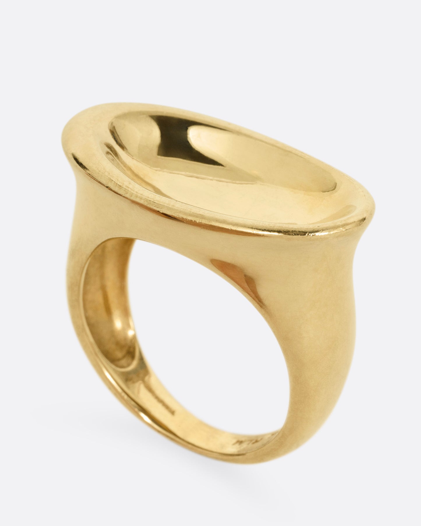A yellow gold ring with a broad oval signet with a slight concave, shown standing up from the side.