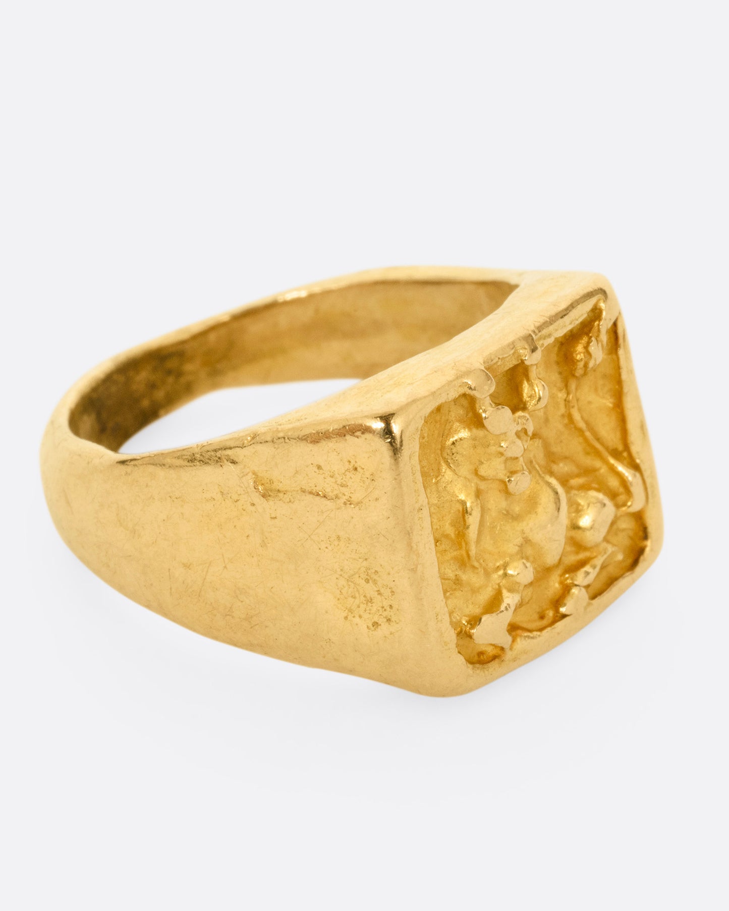 A yellow gold brutalist signet ring with an abstract bull on the front and 'hermano' scrawled on its shoulder, shown from the side.