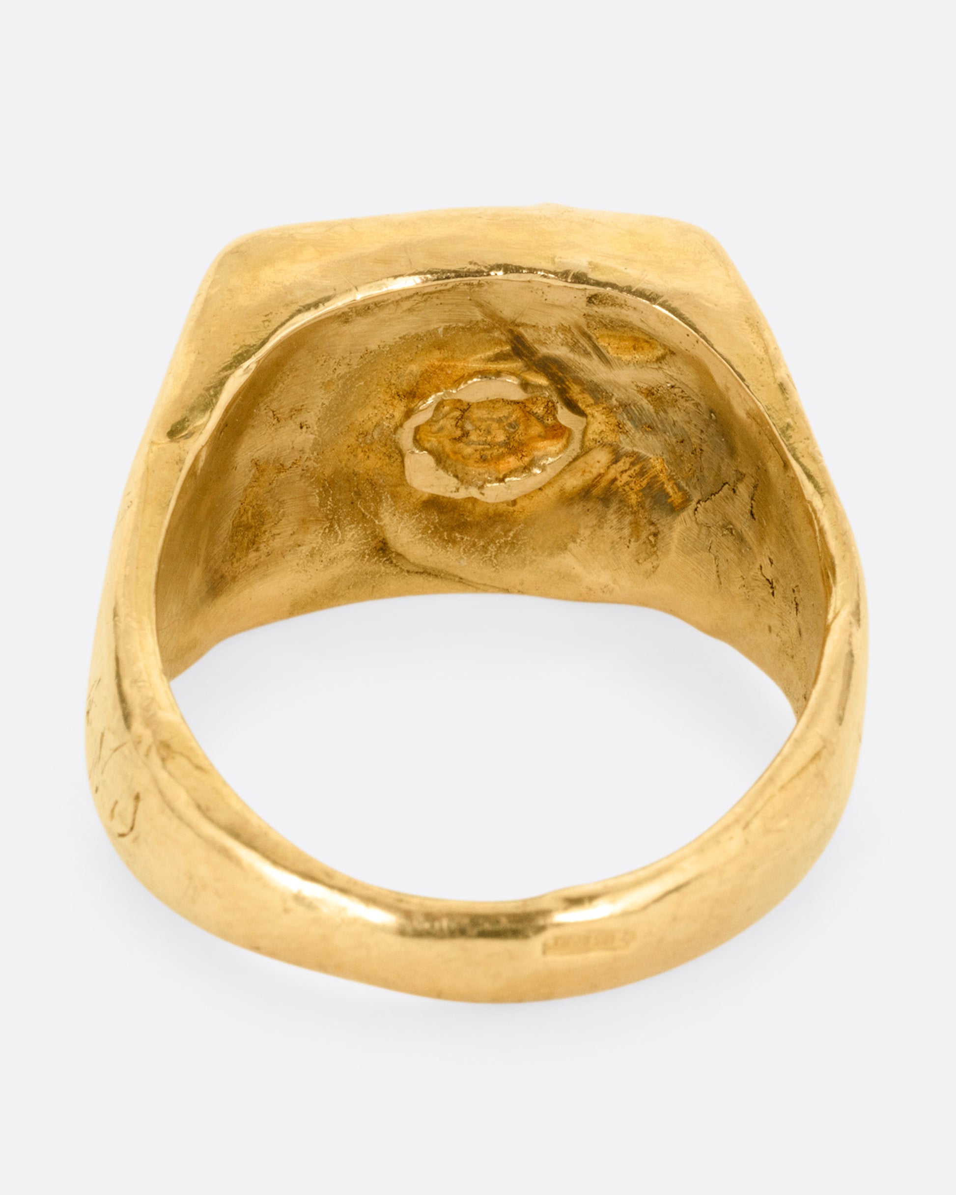 A yellow gold brutalist signet ring with an abstract bull on the front and 'hermano' scrawled on its shoulder, shown from the back.