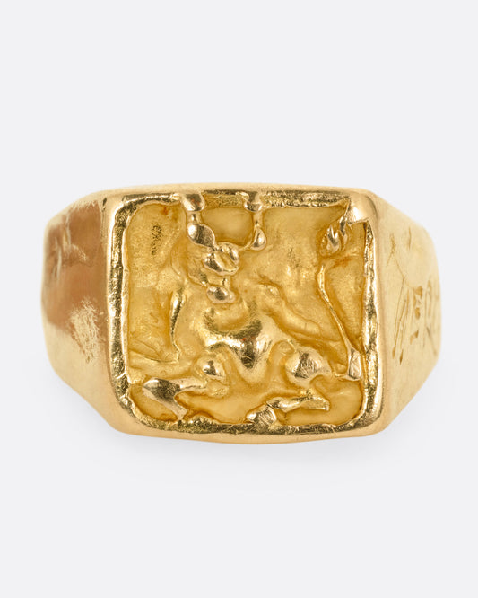 A yellow gold brutalist signet ring with an abstract bull on the front and 'hermano' scrawled on its shoulder, shown from the front.
