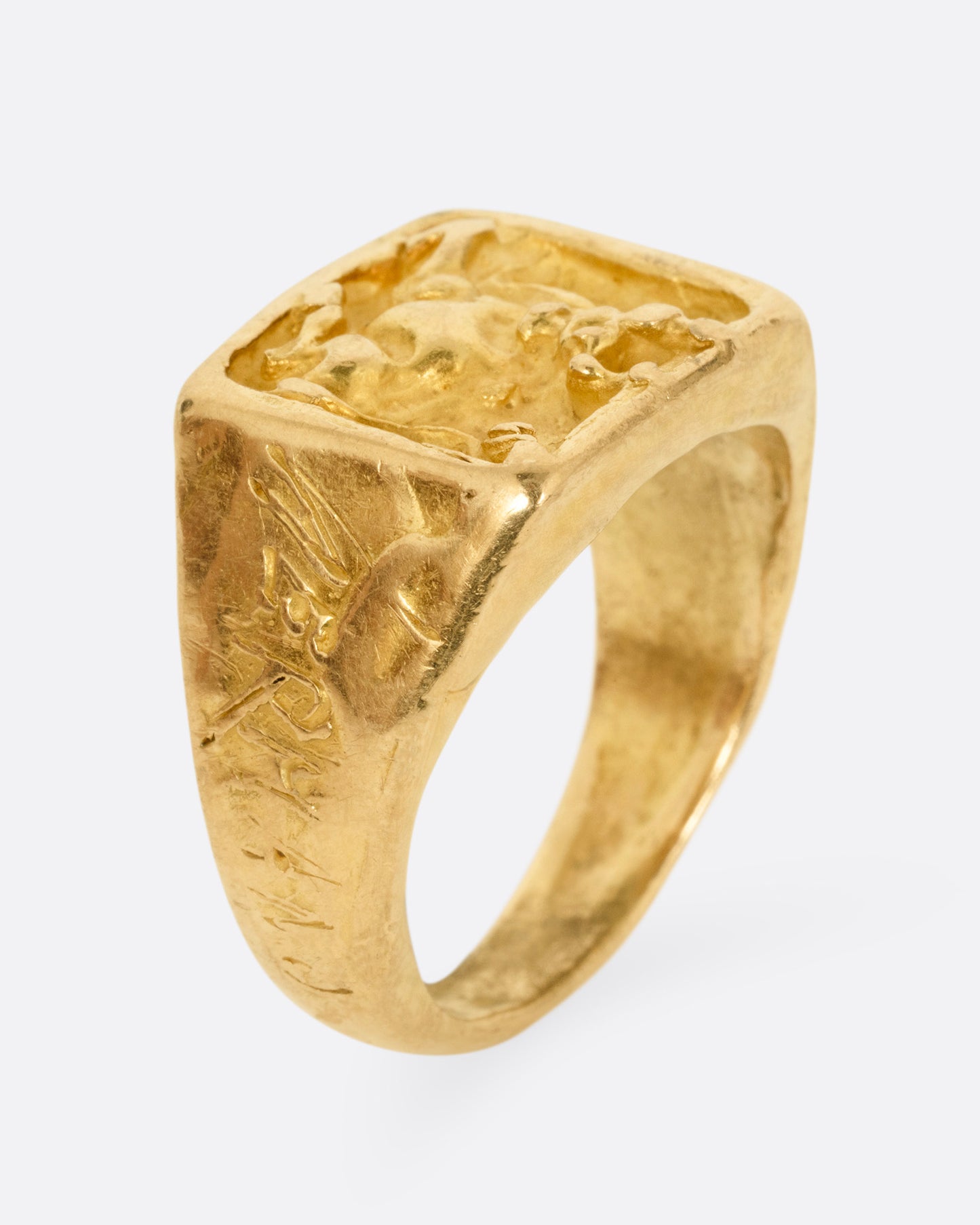 A yellow gold brutalist signet ring with an abstract bull on the front and 'hermano' scrawled on its shoulder, shown from the side standing up.