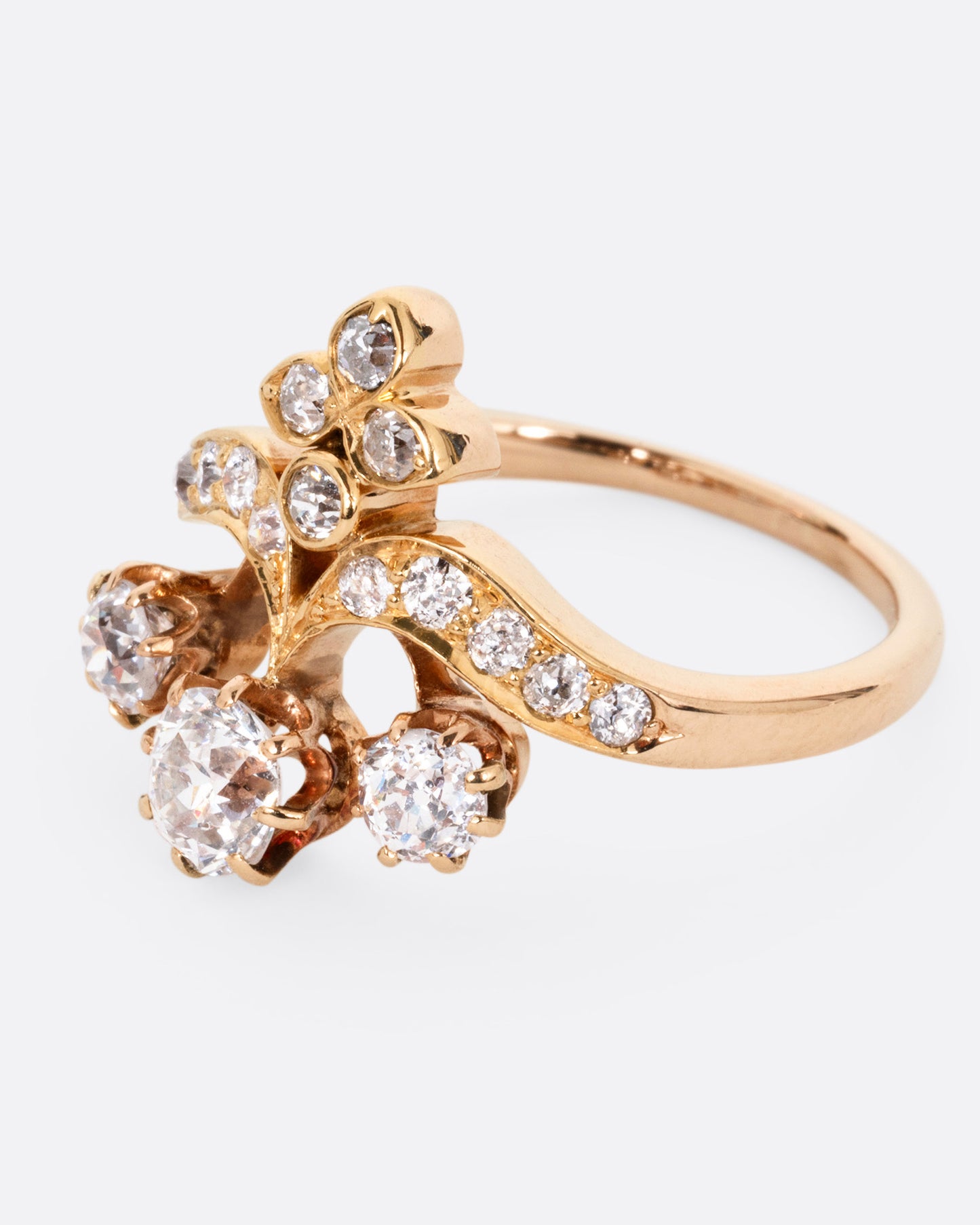 A rose and yellow gold ring with hand cut Old European diamonds in varying sizes, shown from the side.