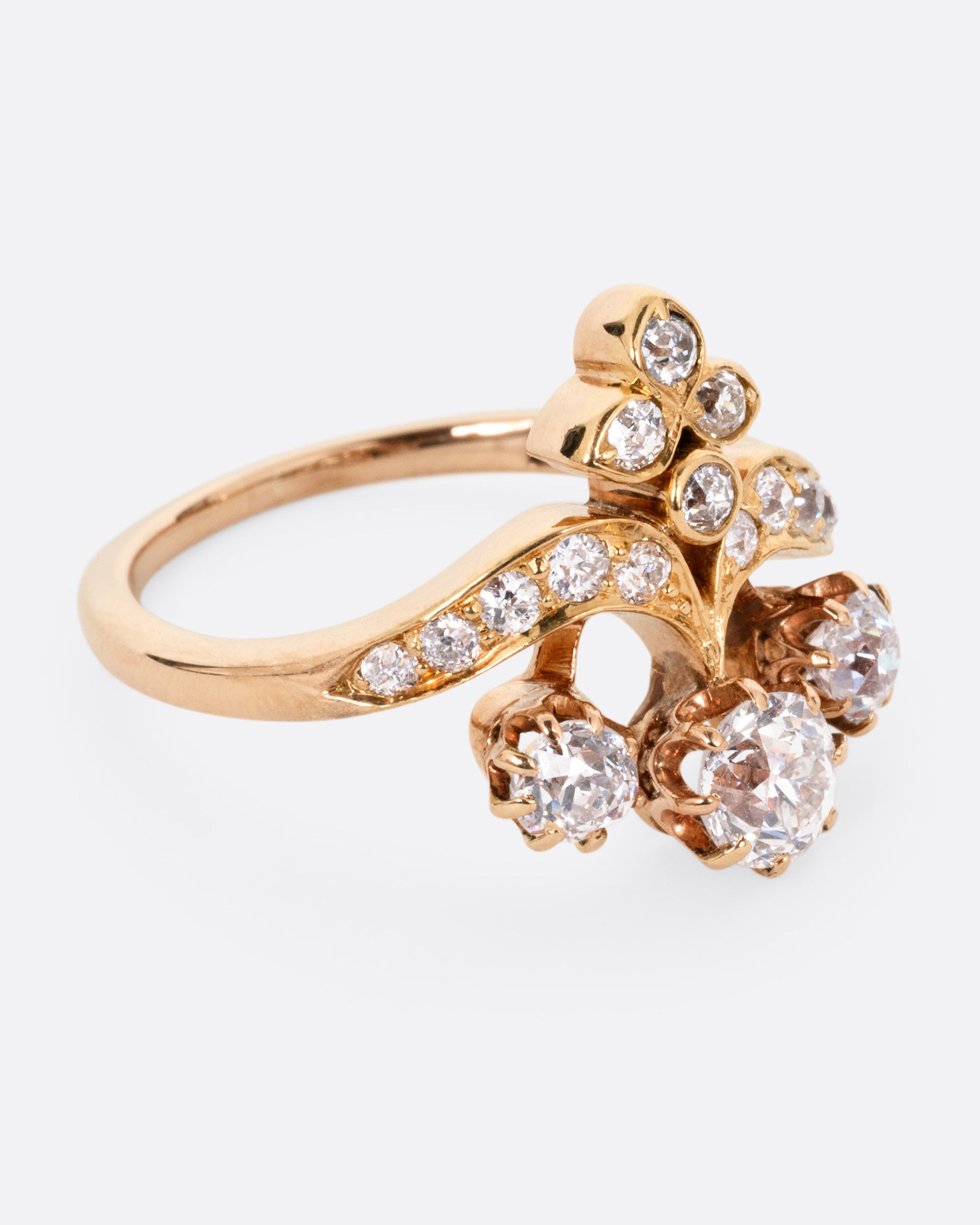 A rose and yellow gold ring with hand cut Old European diamonds in varying sizes, shown from the side.
