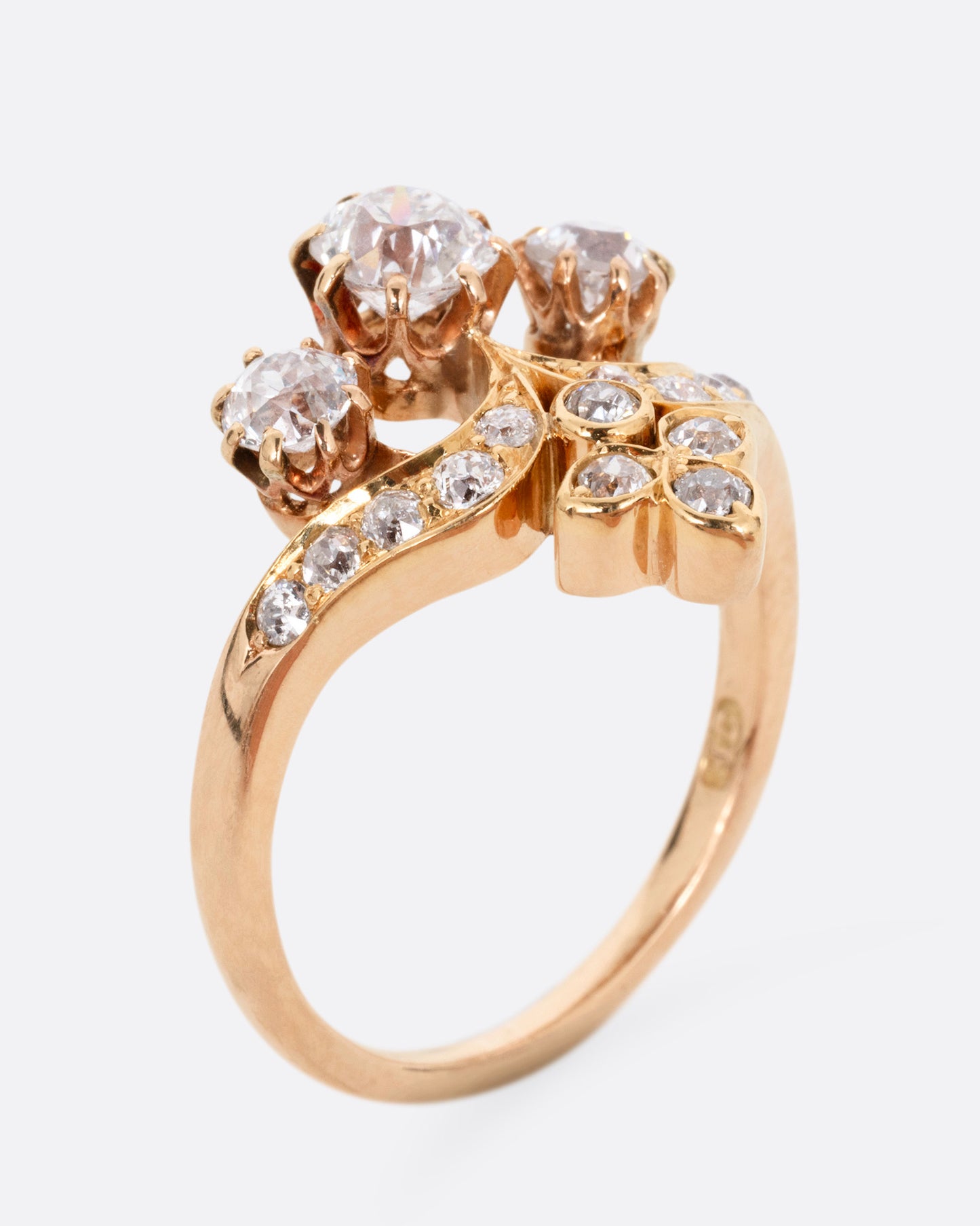 A rose and yellow gold ring with hand cut Old European diamonds in varying sizes, shown from the side standing up.