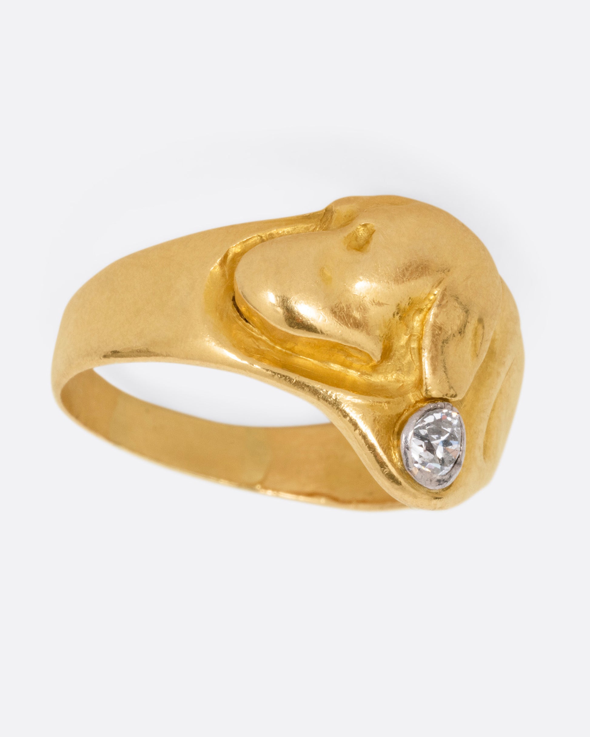 A yellow gold ring with the profile of a dog and a single diamond. Shown from the side.