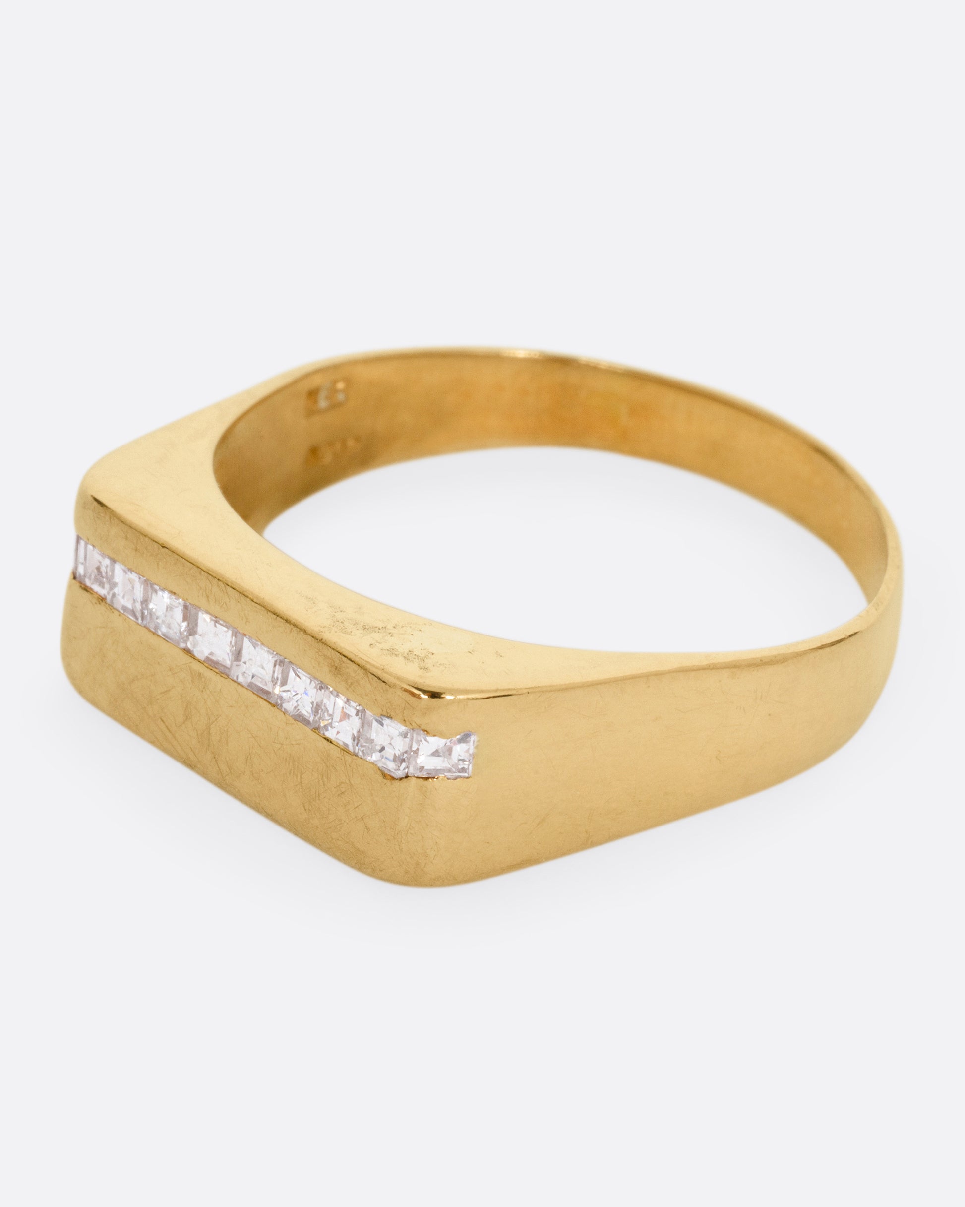 A yellow gold signet ring with a queue of Asscher cut diamonds stretching across the face. Shown from the side.