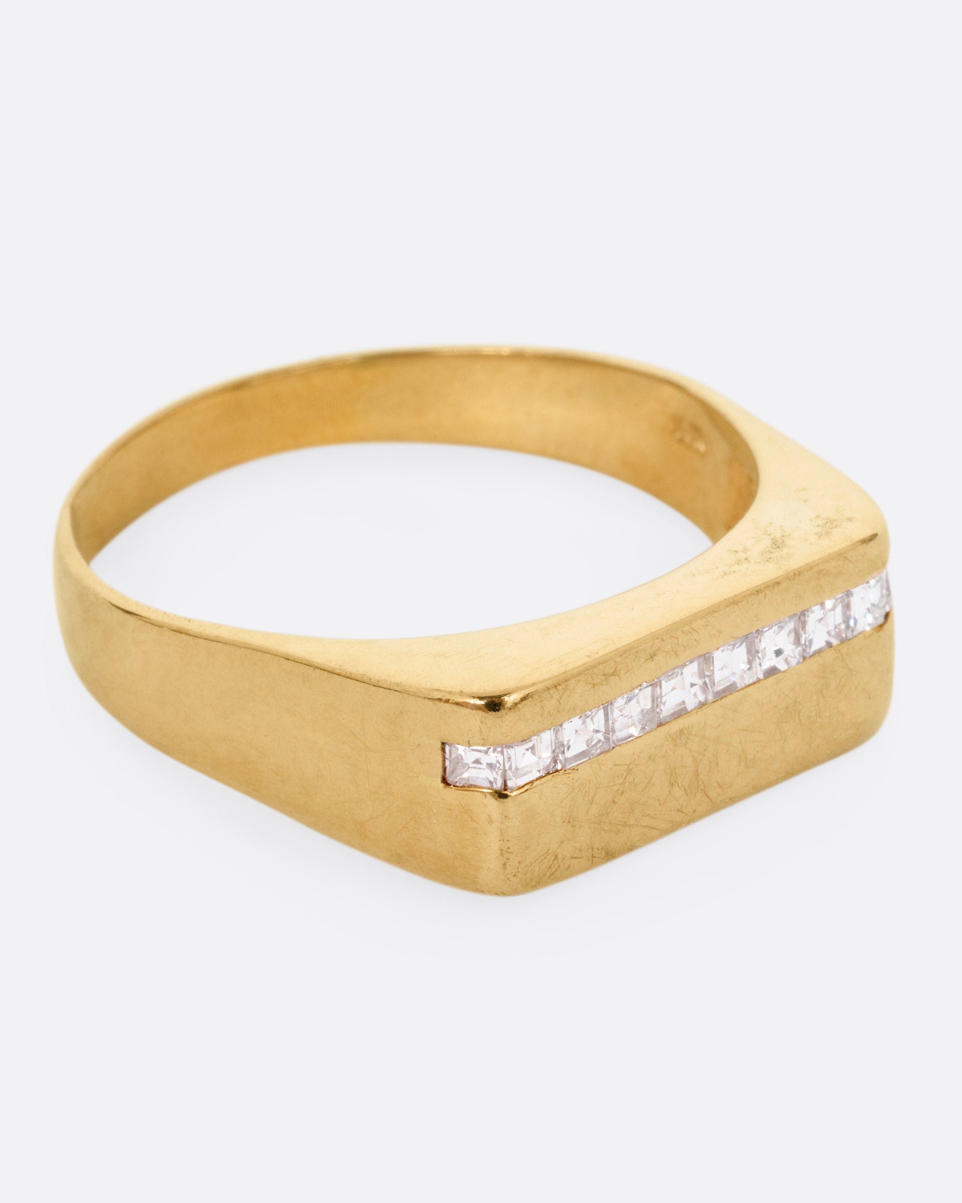 A yellow gold signet ring with a queue of Asscher cut diamonds stretching across the face. Shown from the side.