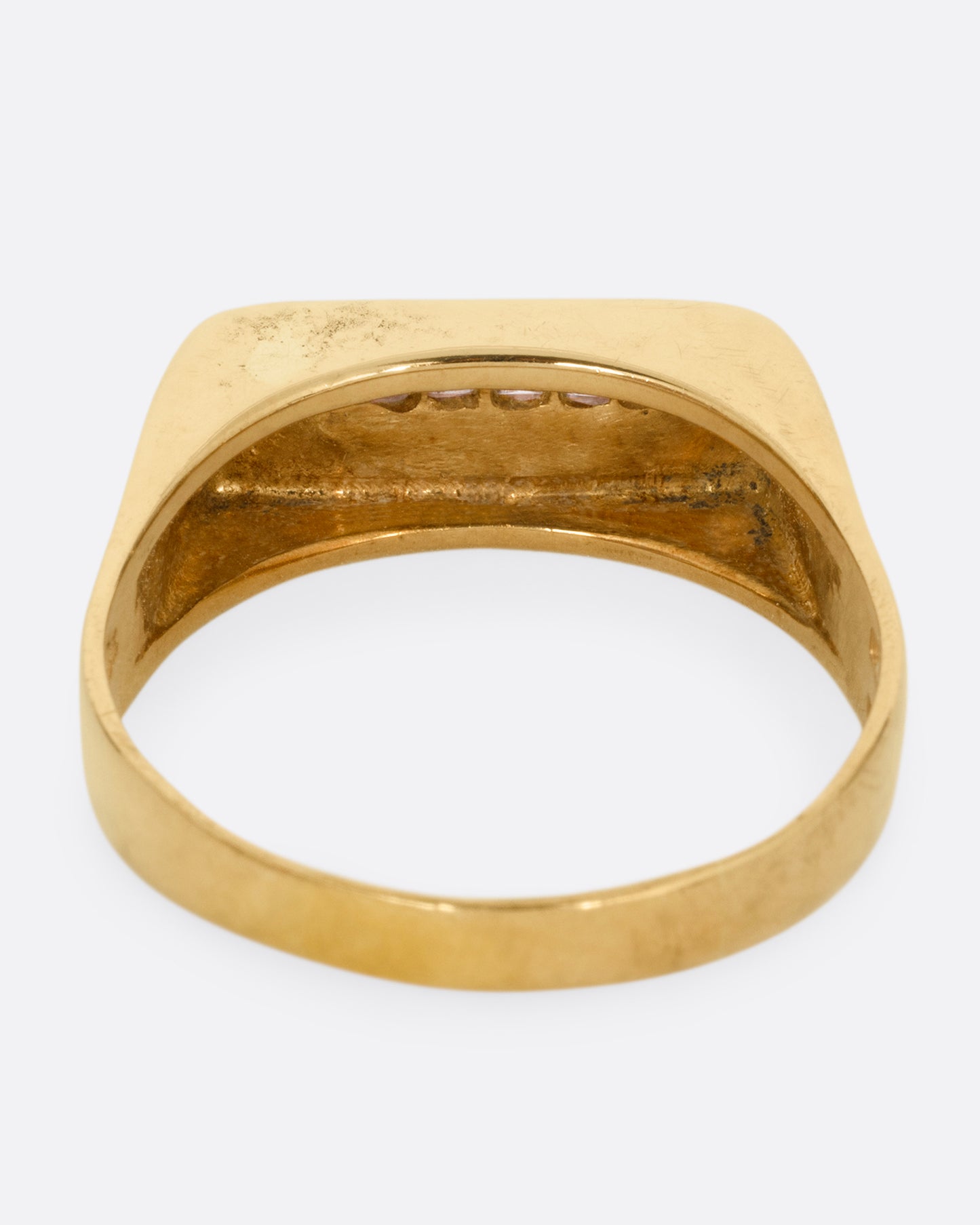 A yellow gold signet ring with a queue of Asscher cut diamonds stretching across the face. Shown from the back.