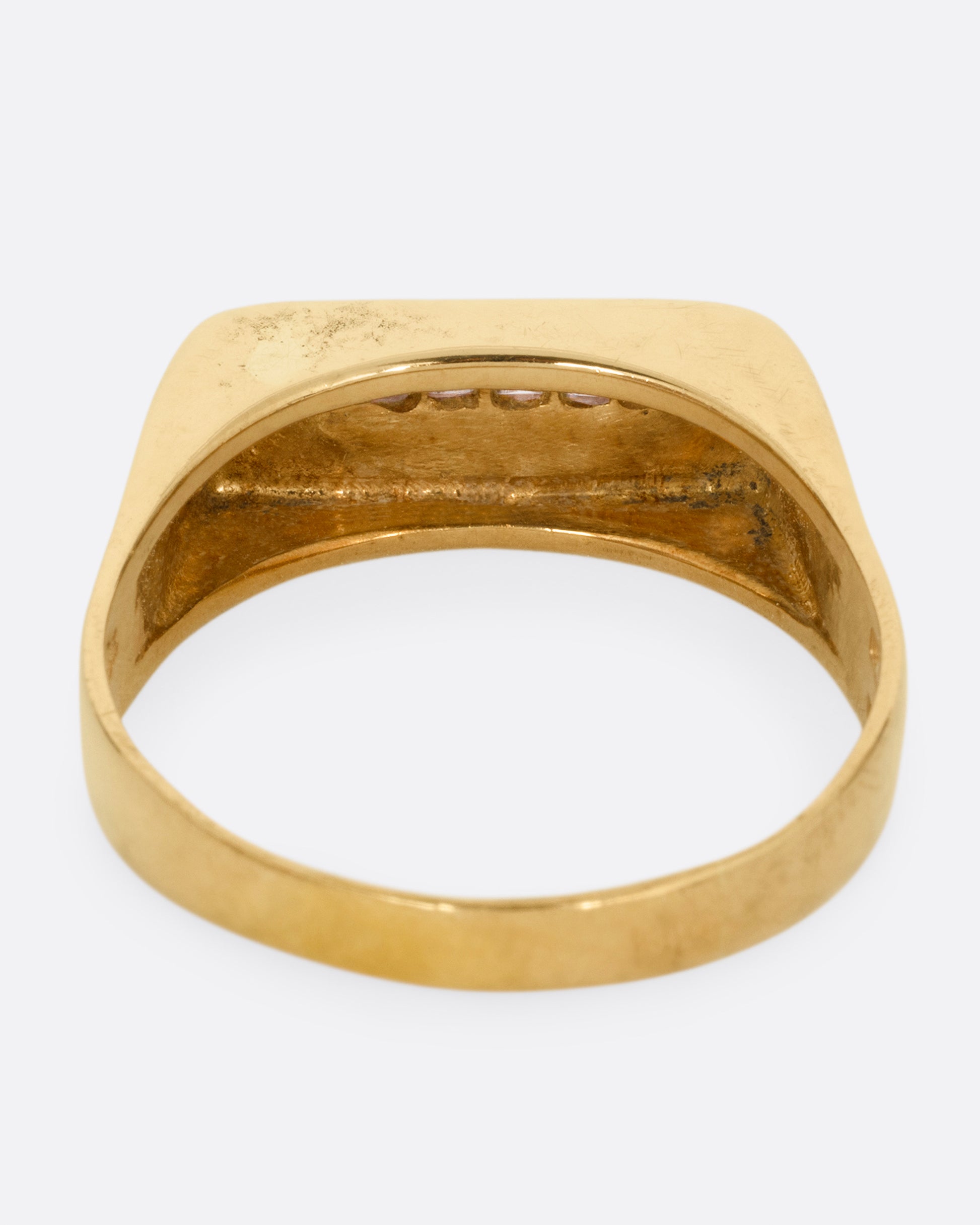 A yellow gold signet ring with a queue of Asscher cut diamonds stretching across the face. Shown from the back.