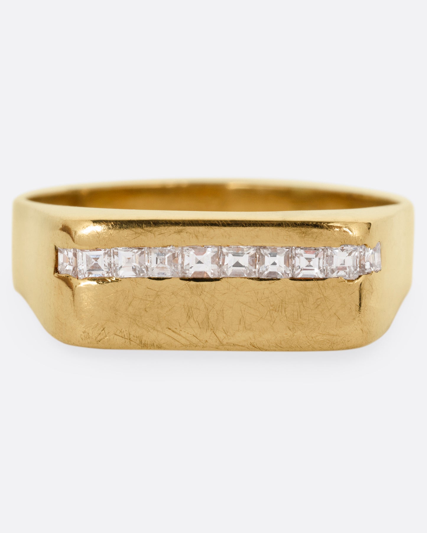 A yellow gold signet ring with a queue of Asscher cut diamonds stretching across the face. Shown from the front.
