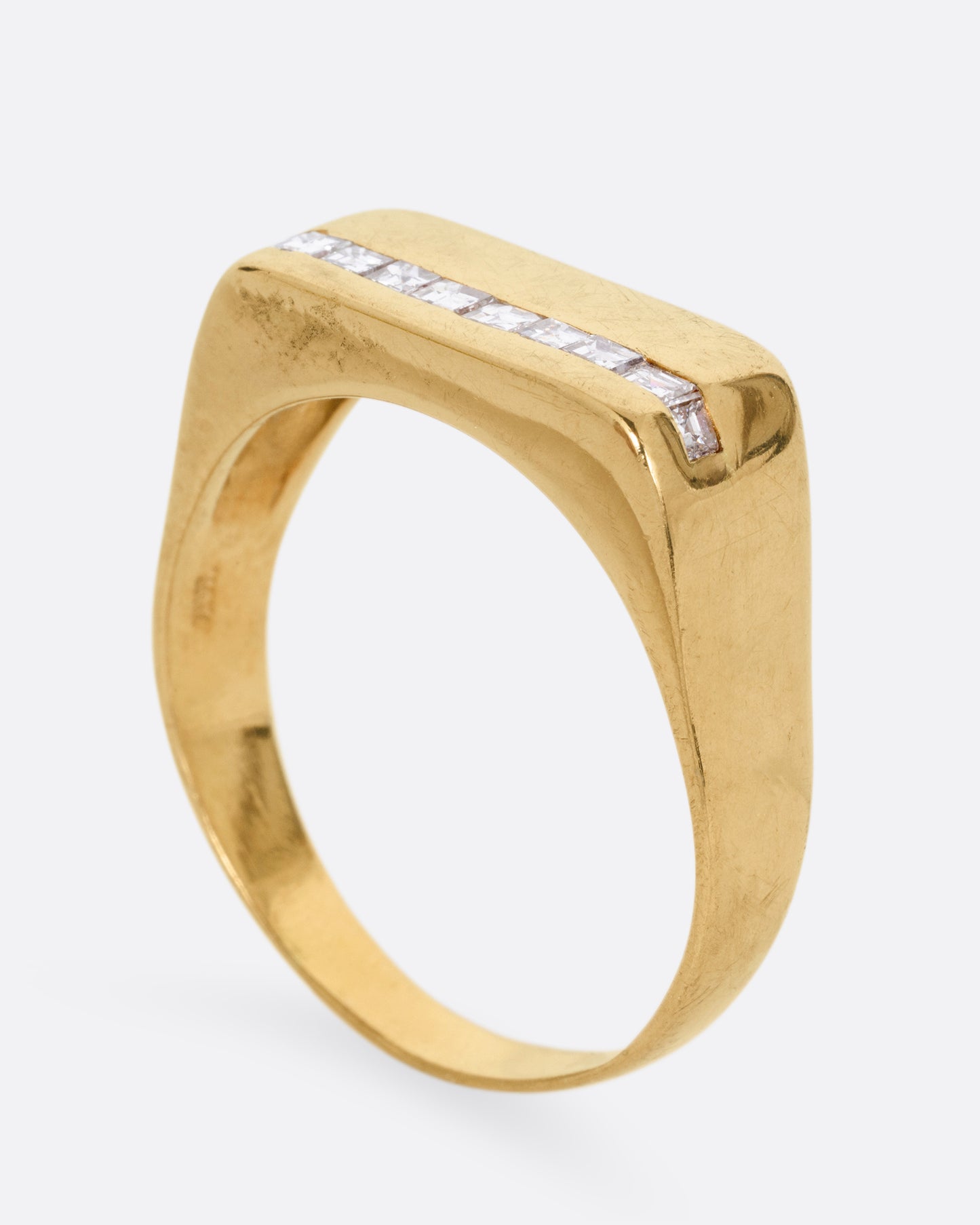 A yellow gold signet ring with a queue of Asscher cut diamonds stretching across the face. Shown from the side standing up.