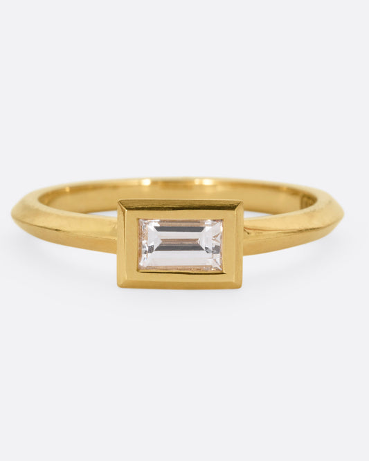 A yellow gold ring with a baguette diamond, shown from the front.