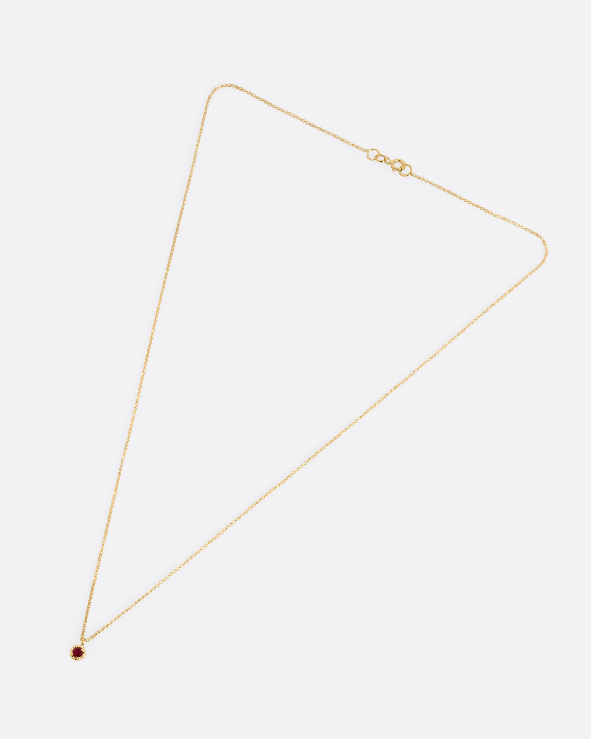 A yellow gold cable chain necklace with a  prong set ruby, shown from the front.