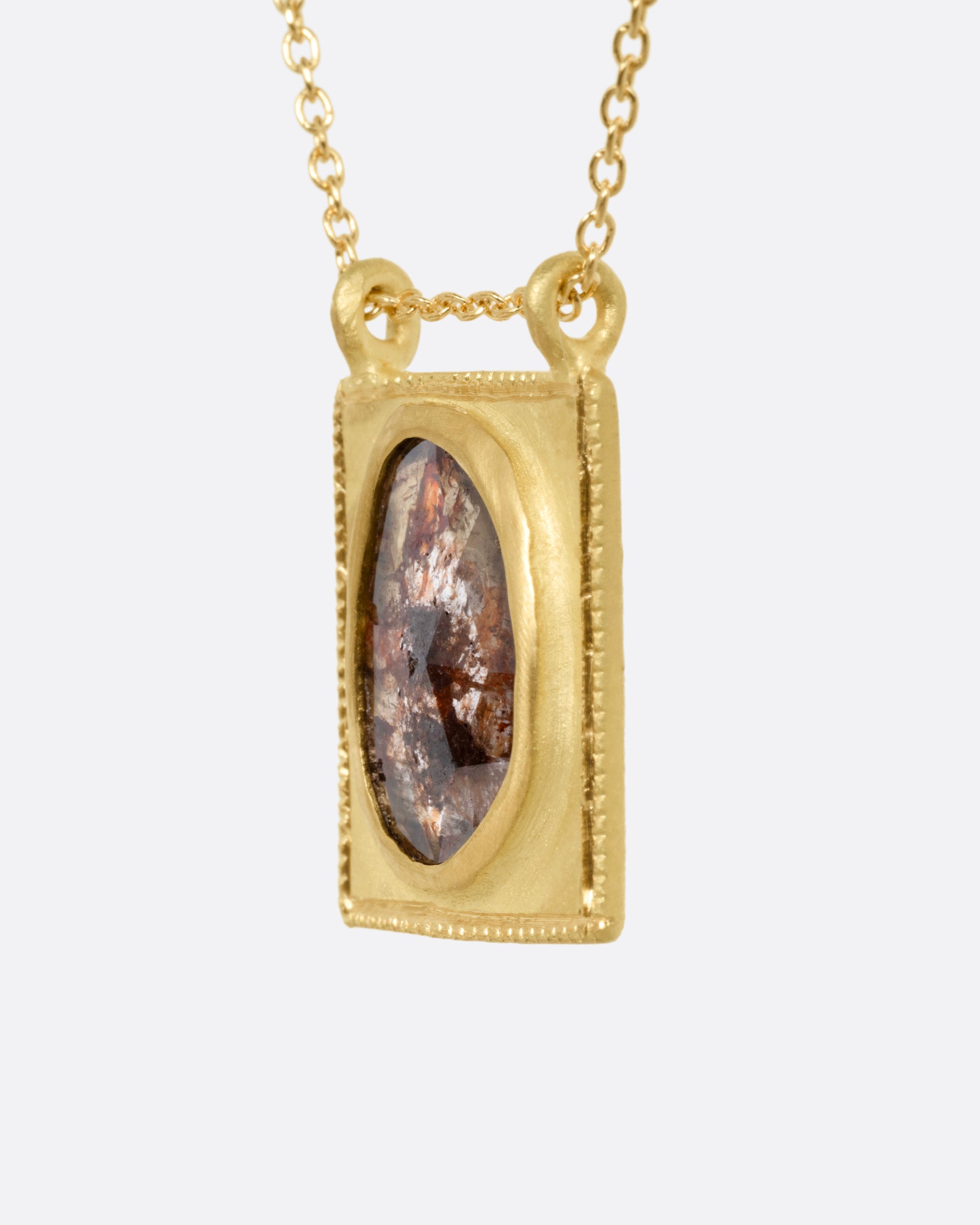 A yellow gold pendant necklace with a rose cut salt and pepper diamond in a rectangular gold frame, with a double bail. Shown from the side.