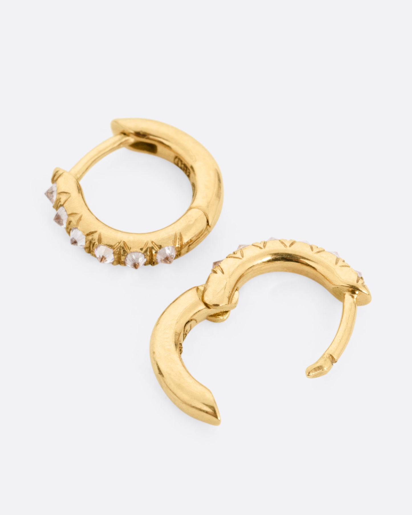 A pair of yellow gold hoop earrings with reverse set diamonds. Shown lying on their sides with one hoop open.