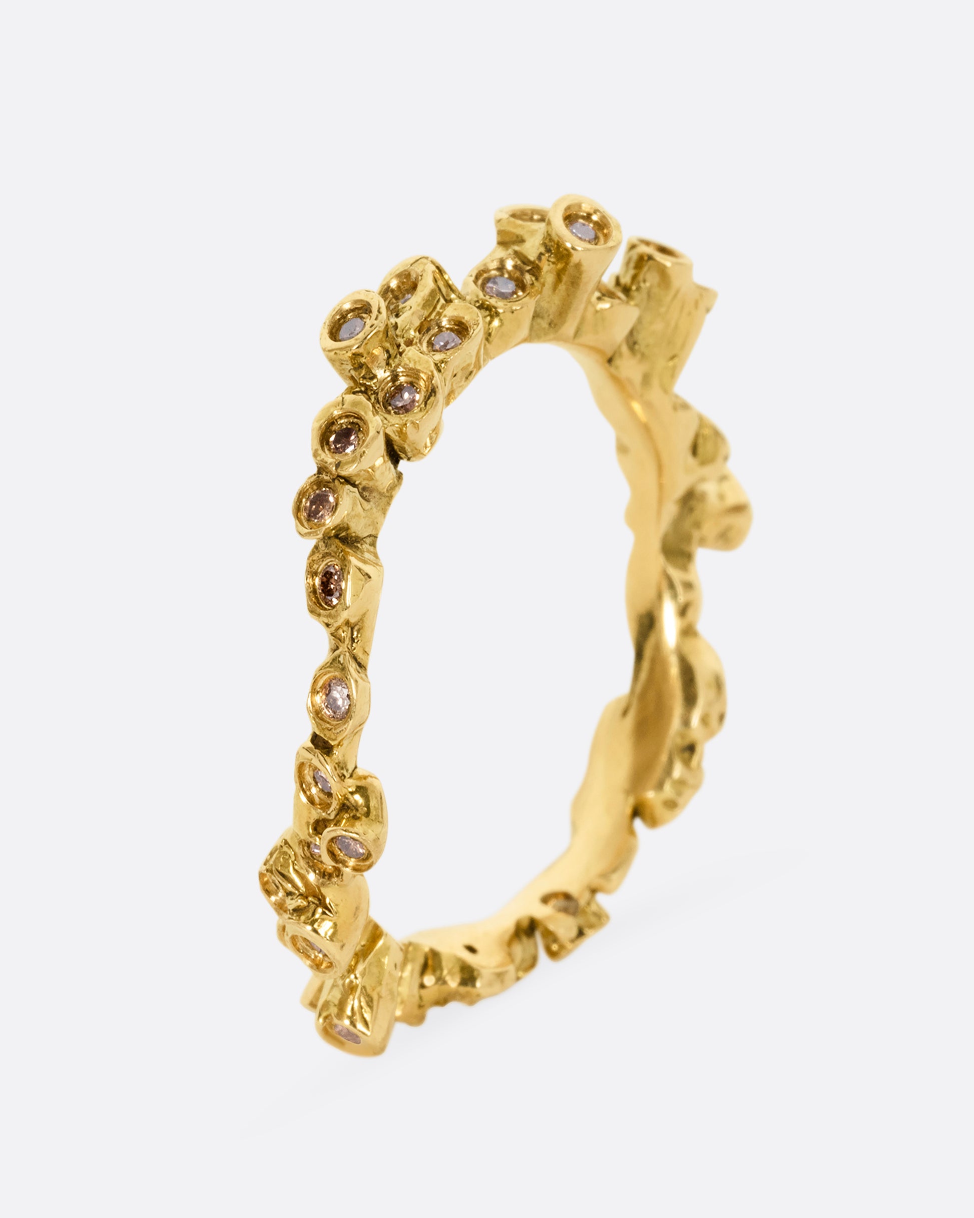 A yellow gold ring with cognac diamonds in protruding bezel settings that wrap around the entire band. Shown from the side.