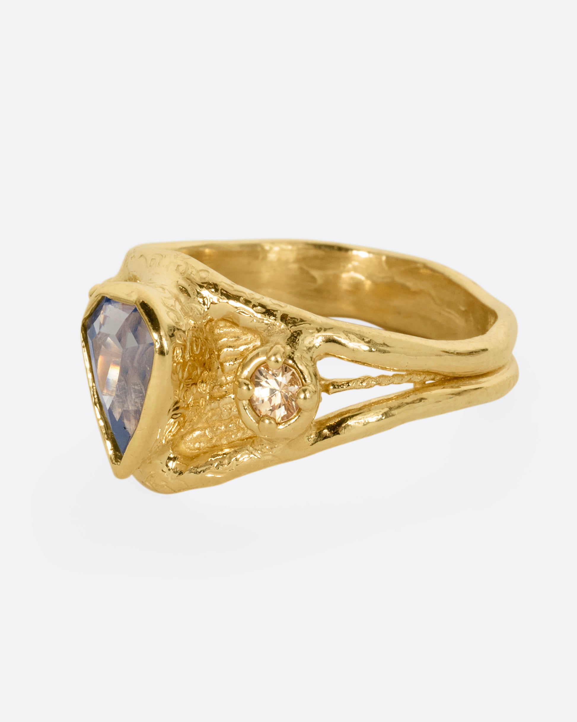 A yellow gold ring with a blue kite shaped sapphire and two yellow sapphires. Shown from the side.