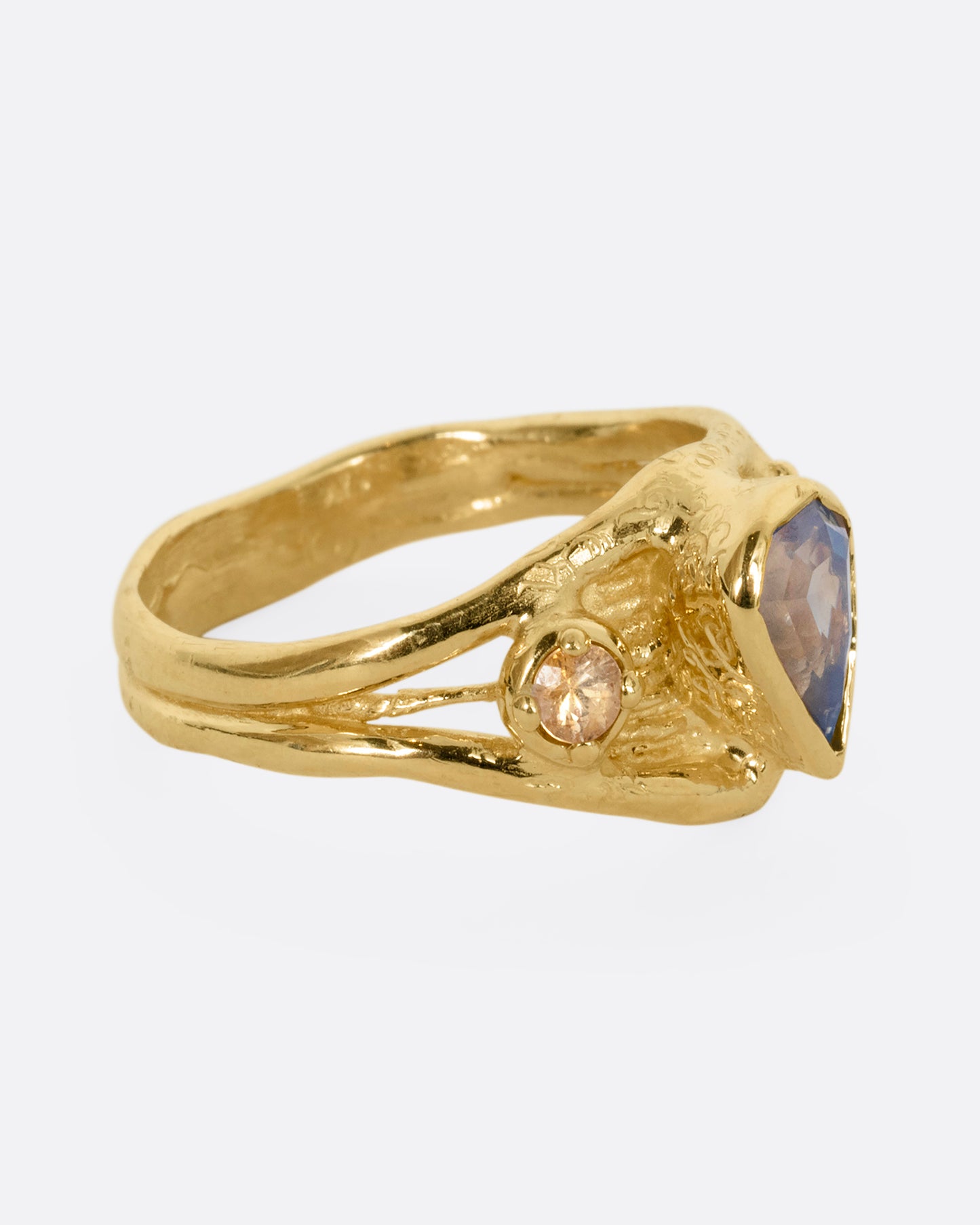 A yellow gold ring with a blue kite shaped sapphire and two yellow sapphires. Shown from the side.