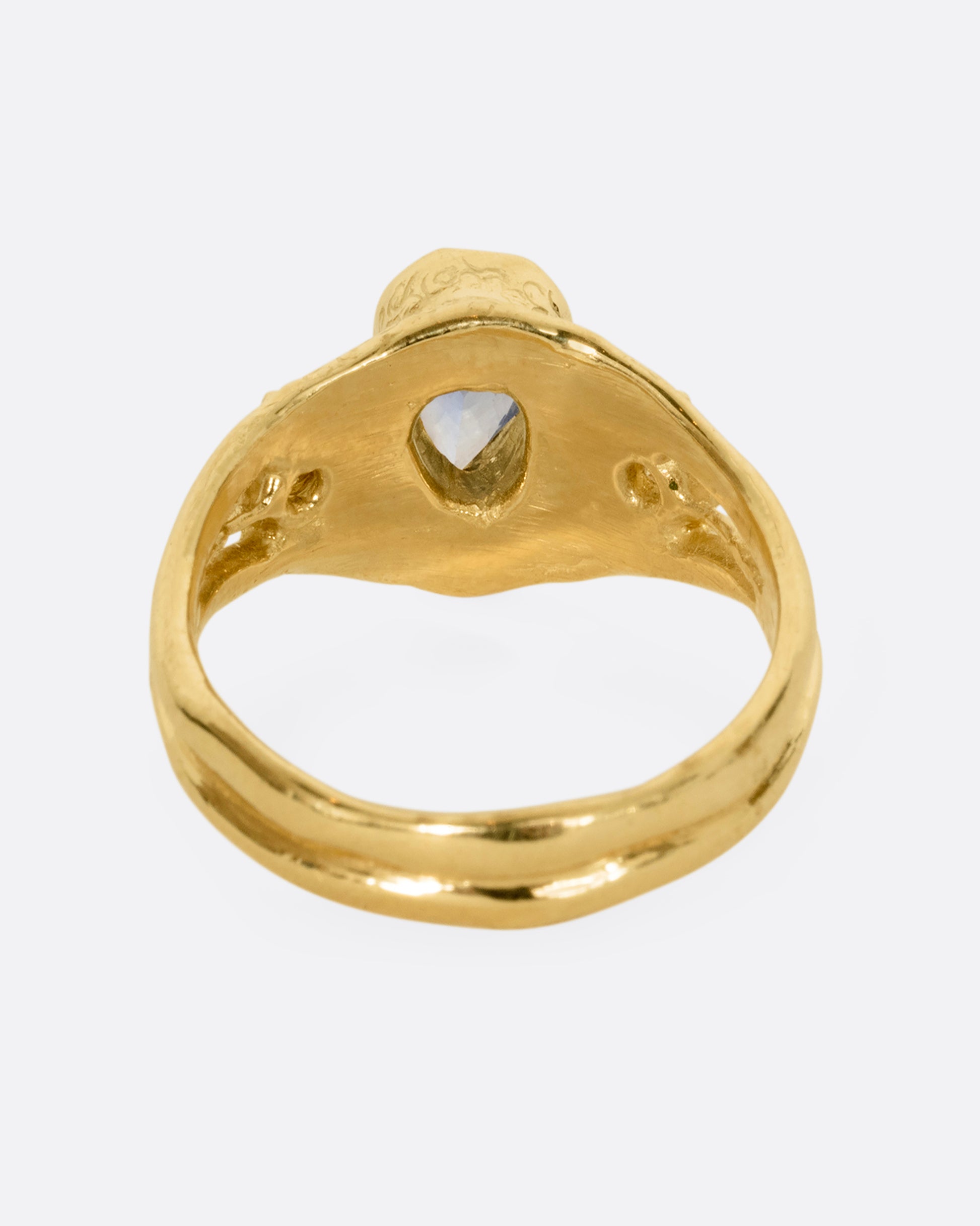 A yellow gold ring with a blue kite shaped sapphire and two yellow sapphires. Shown from the back.