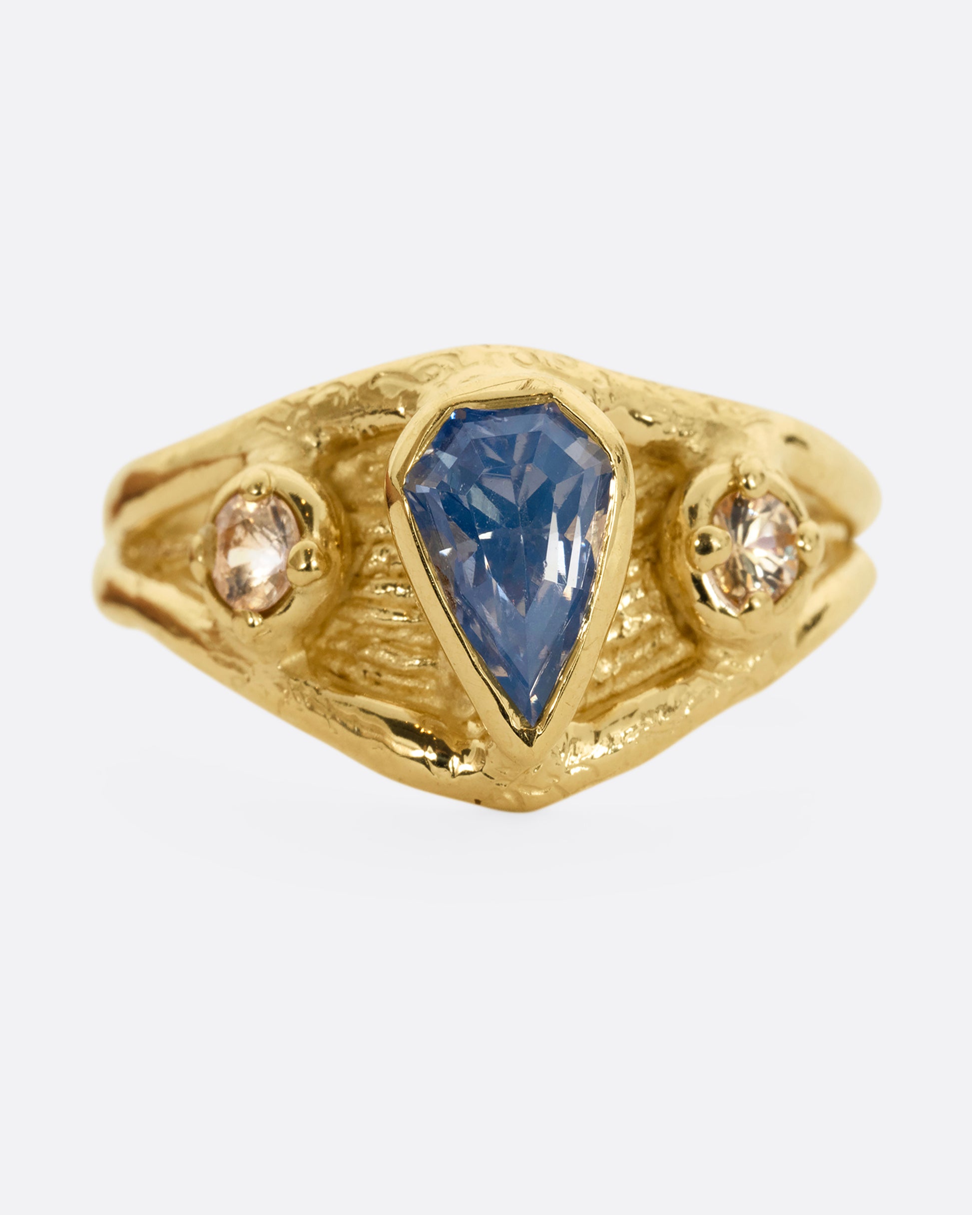A yellow gold ring with a blue kite shaped sapphire and two yellow sapphires. Shown from the front.