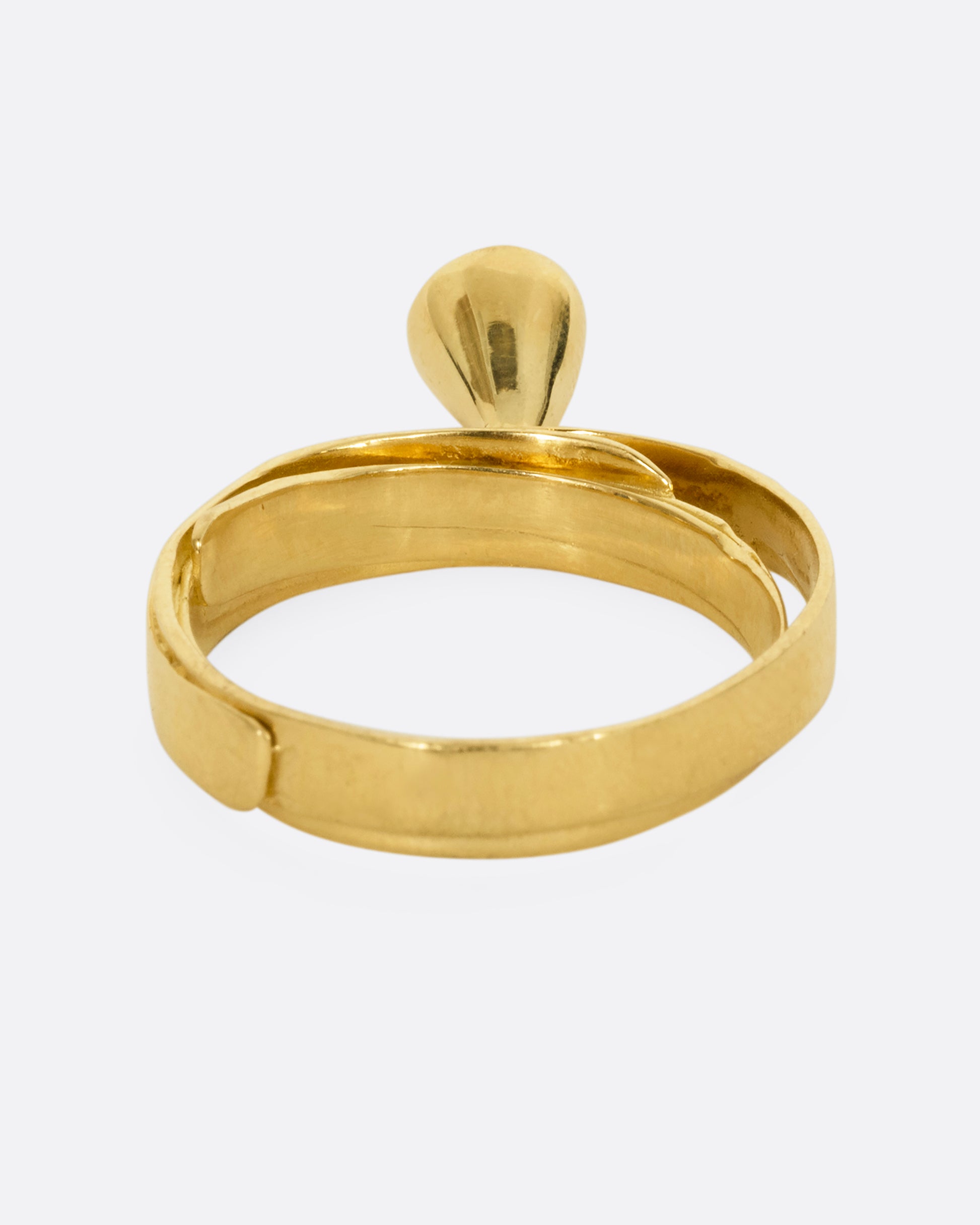 A yellow gold ring that loops over itself twice with a tall bezel set diamond at its center. Shown from the back.