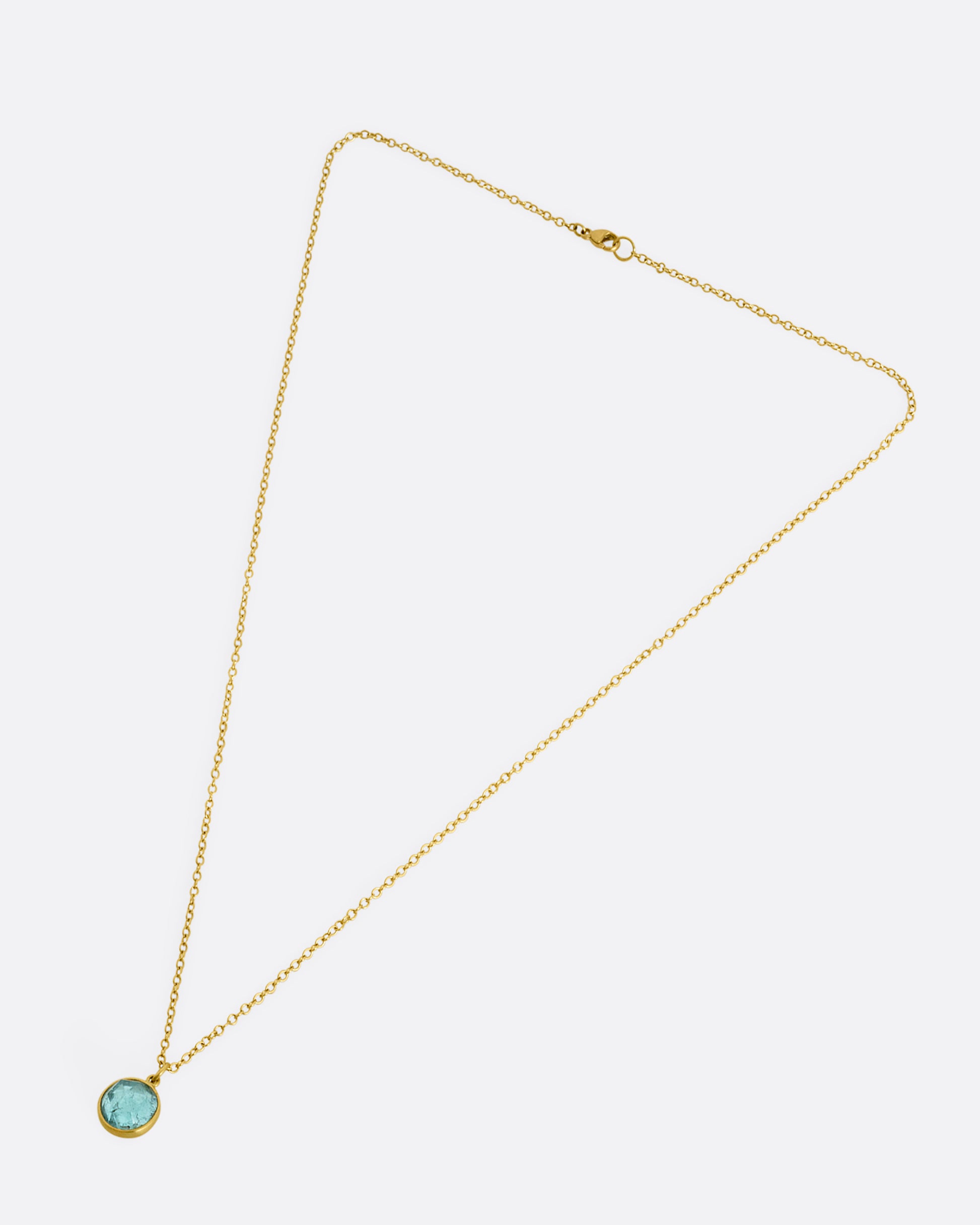 A yellow gold necklace with a circular light blue tourmaline pendant. Shown laying flat.