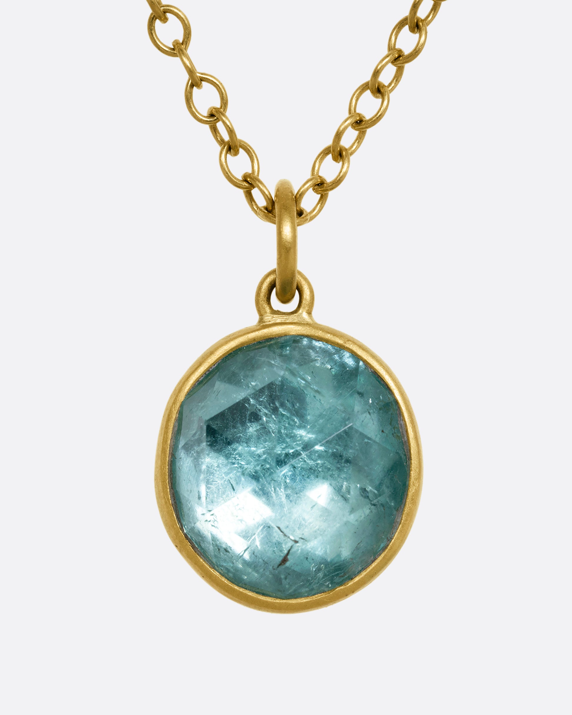 A yellow gold necklace with a circular light blue tourmaline pendant. Shown from the front.