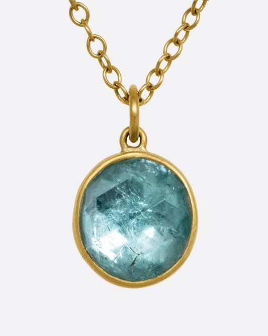 A yellow gold necklace with a circular light blue tourmaline pendant. Shown from the front.
