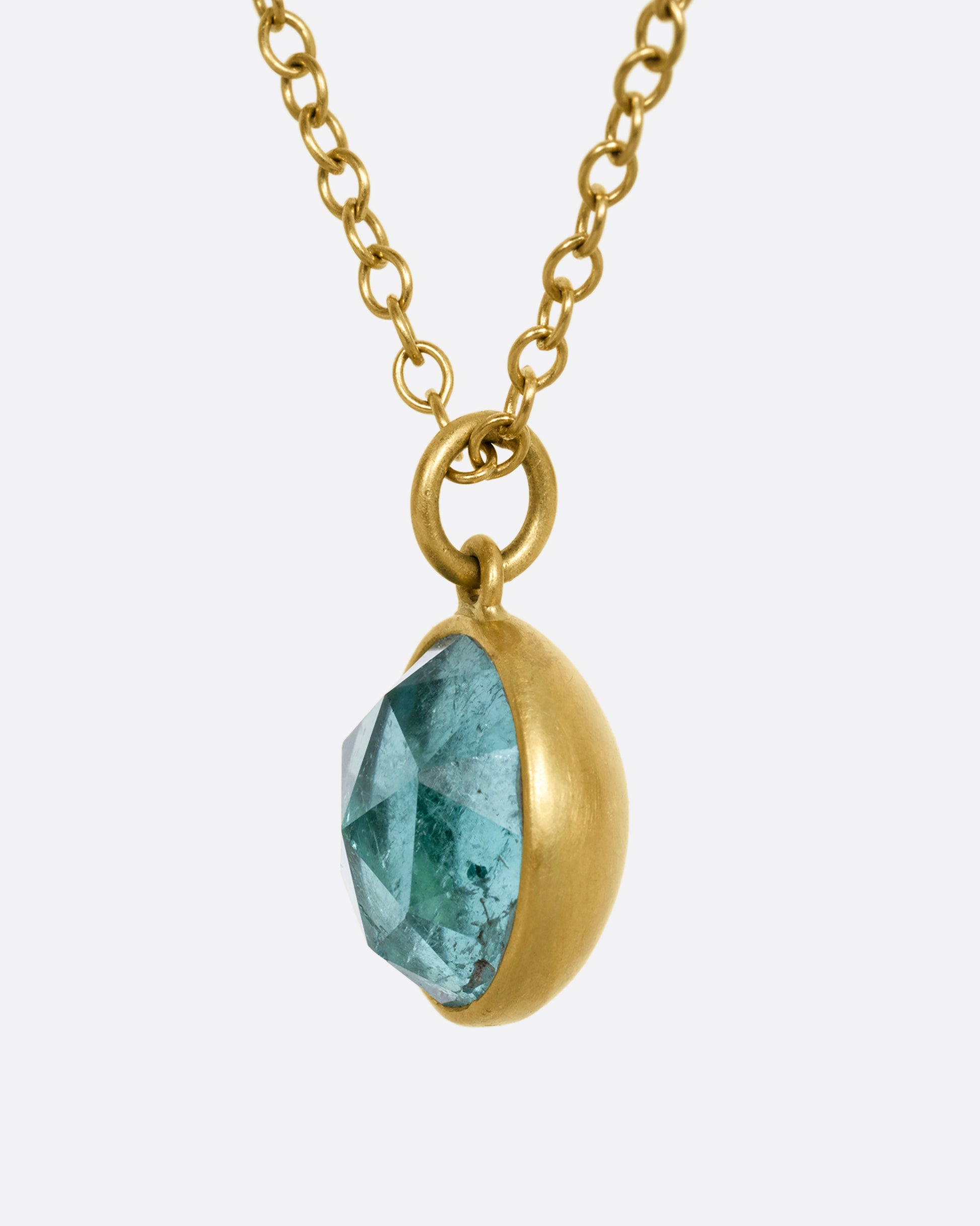 A yellow gold necklace with a circular light blue tourmaline pendant. Shown from the side.