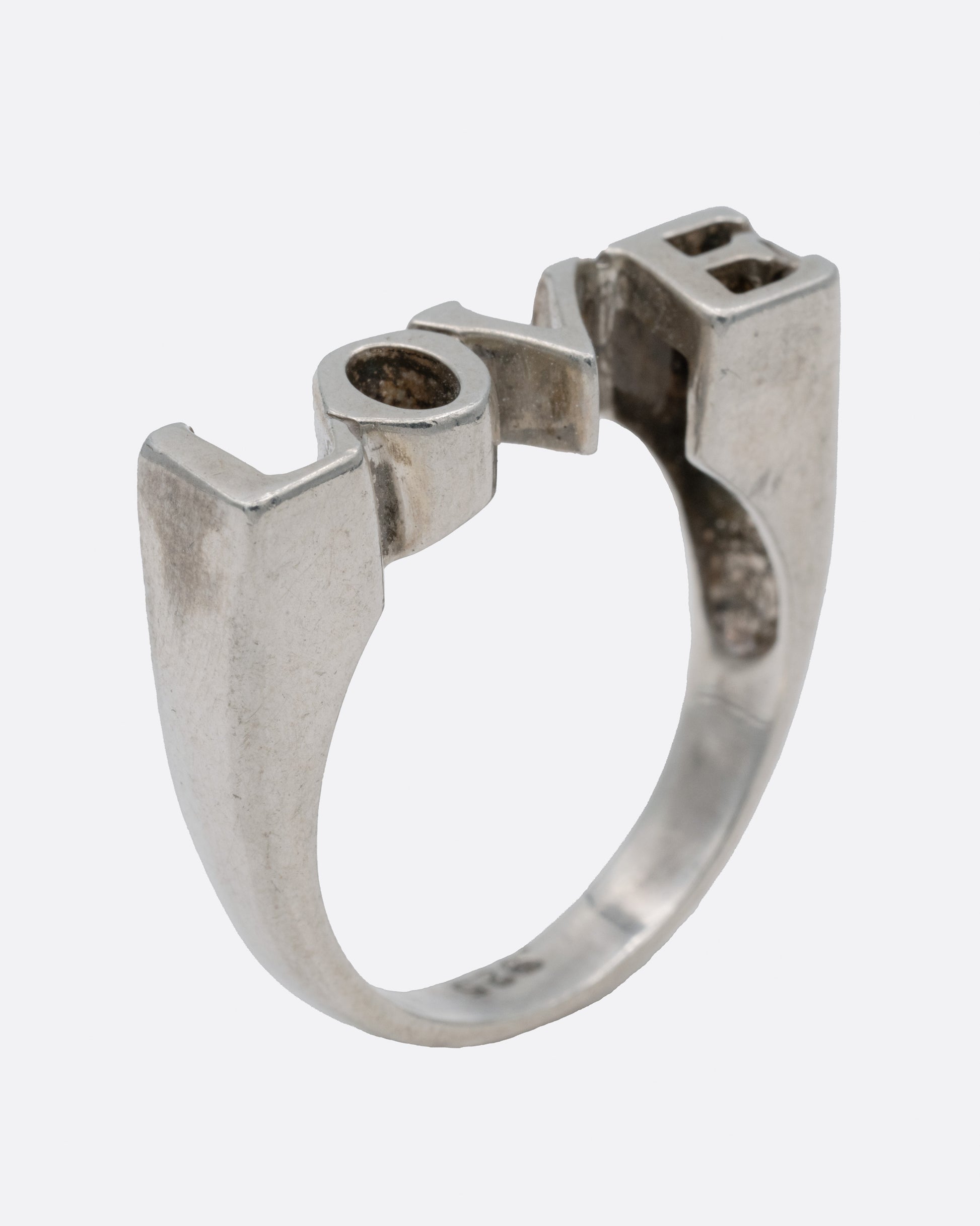 A silver ring with the letters LOVE, shown from the side standing up.