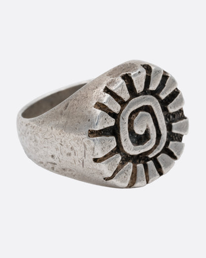 A silver ring with a graphic spiral sun, shown from the side.