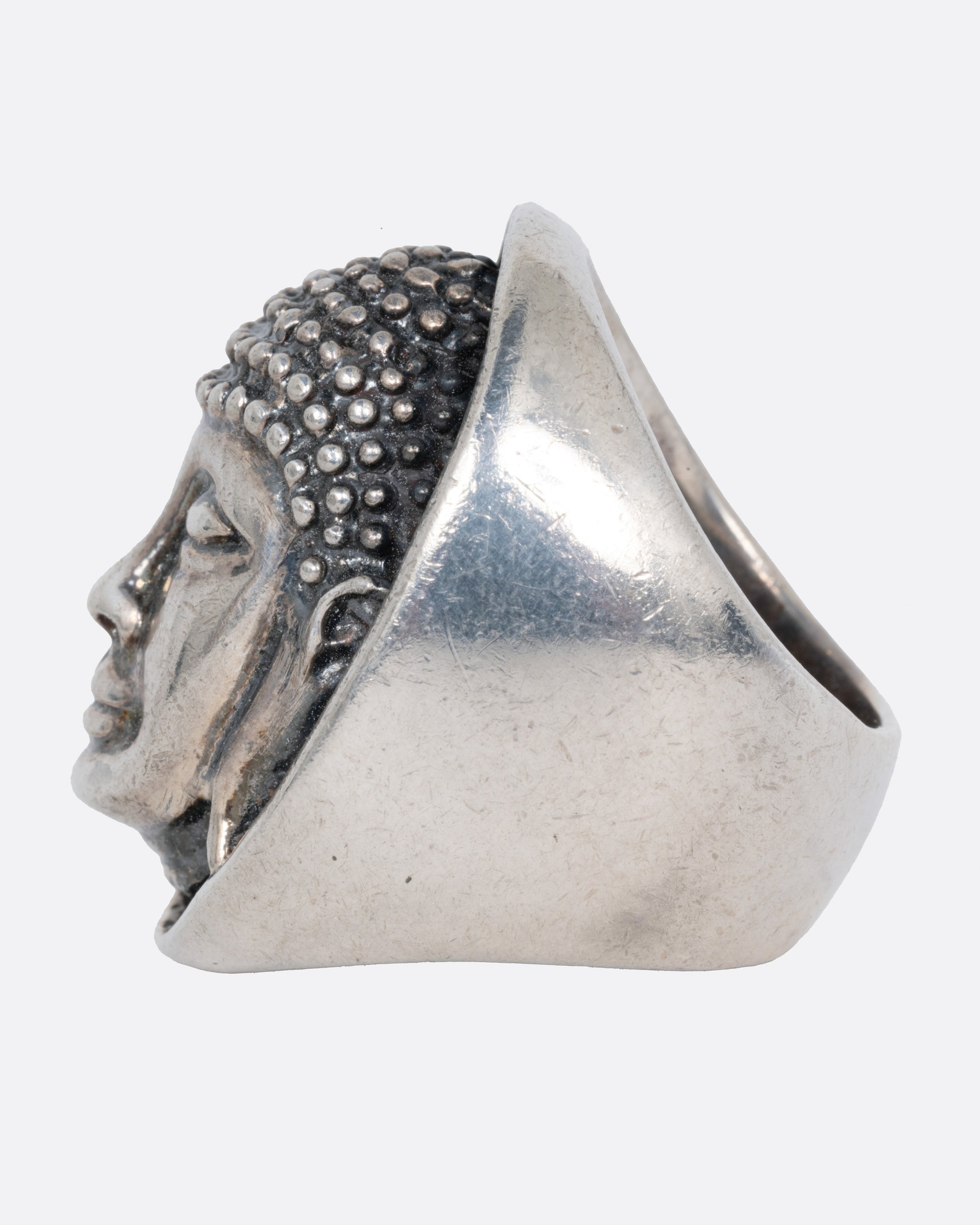 A silver ring with the Buddha's face. Shown from the side.