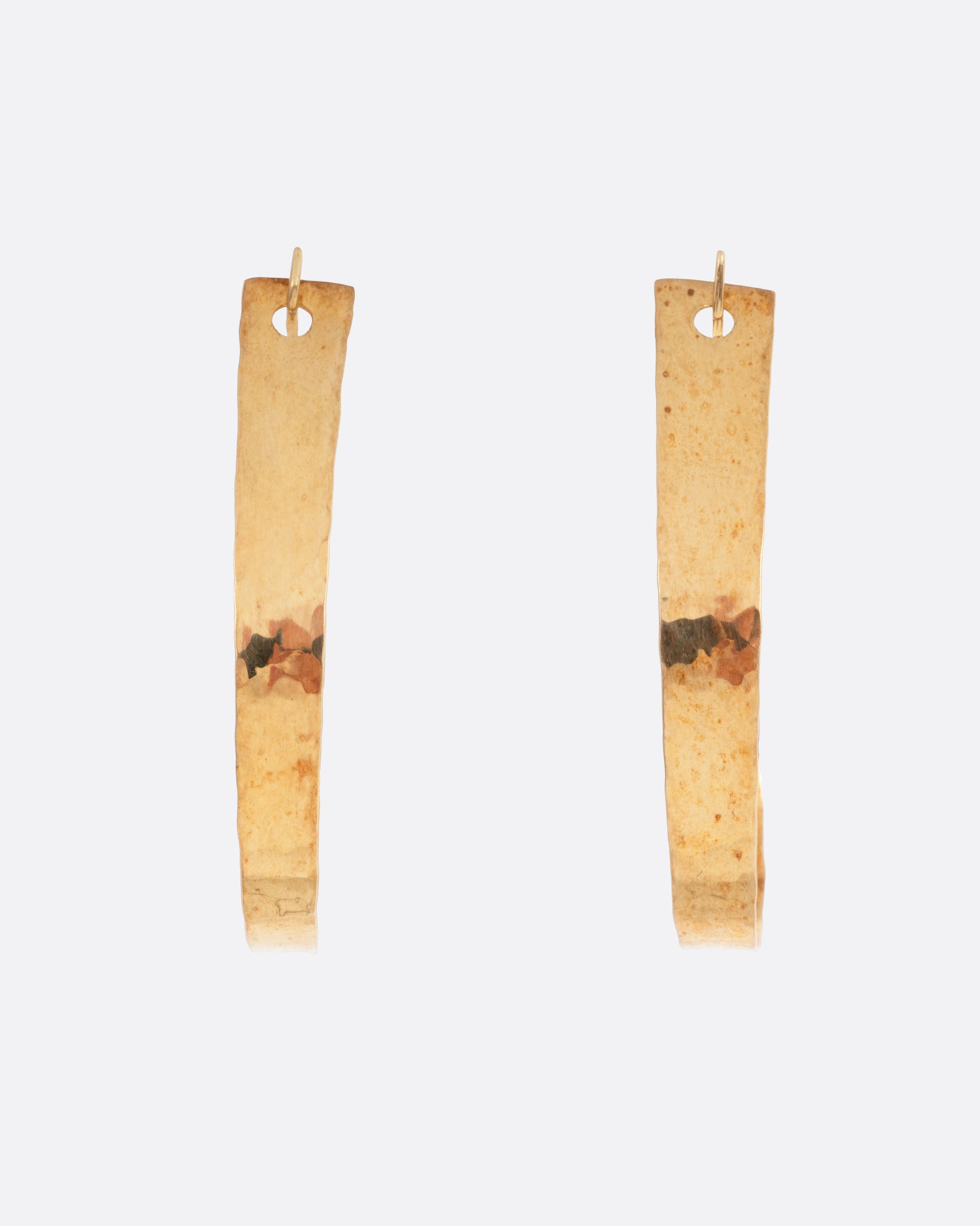 A pair of yellow gold loop earrings with a tapered silhouette and minimalist closure, shown from the front.