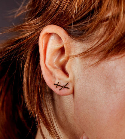 Gold crossed bar stud earrings worn on an ear